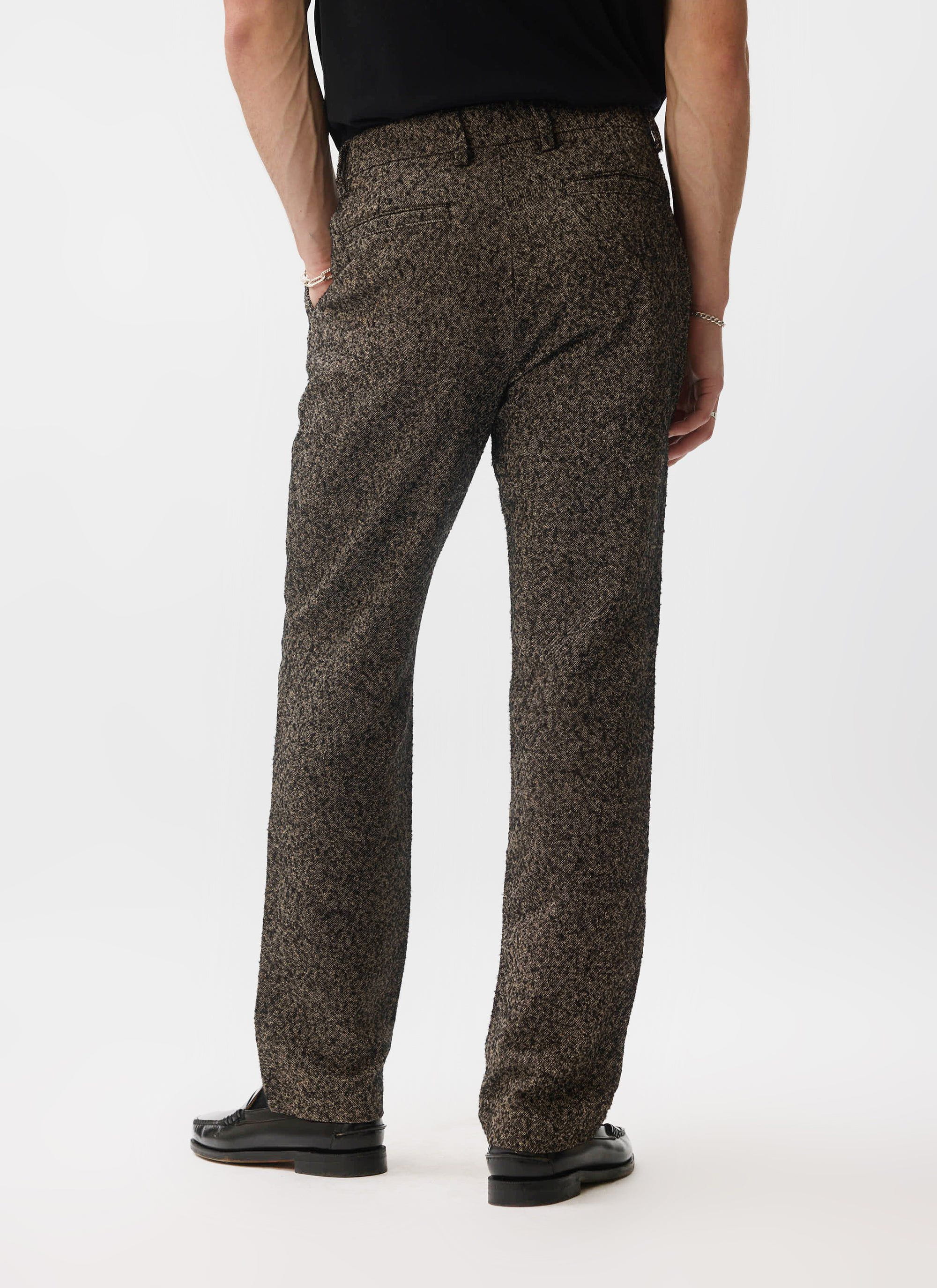 A rear view of a model wearing the Percival Blyton Trousers in a warm grey nep fabric with black loafers.