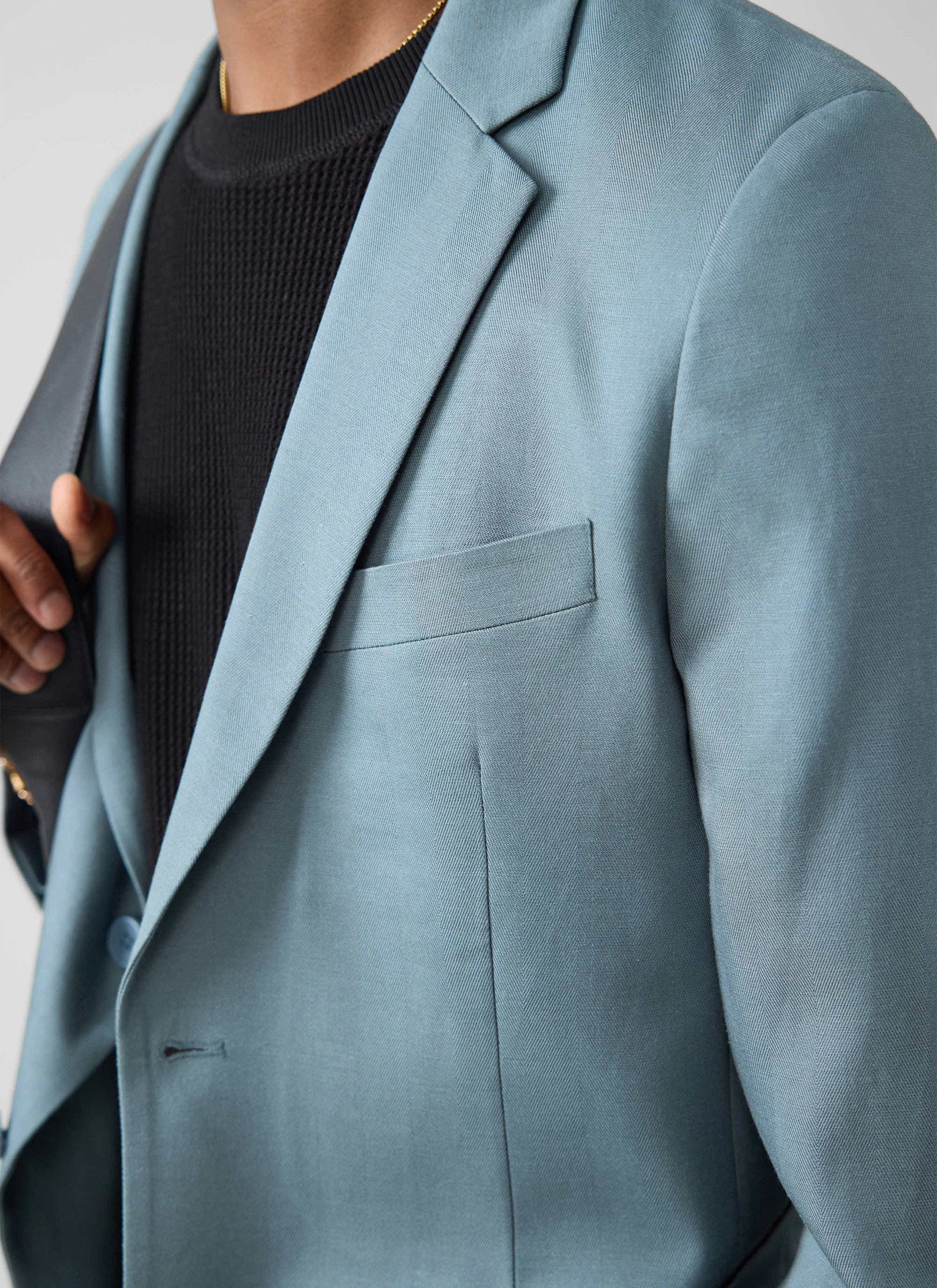 Close-up of a model wearing the Percival Lyocell Regular Blazer in Slate Blue, styled over a black knitted jumper.