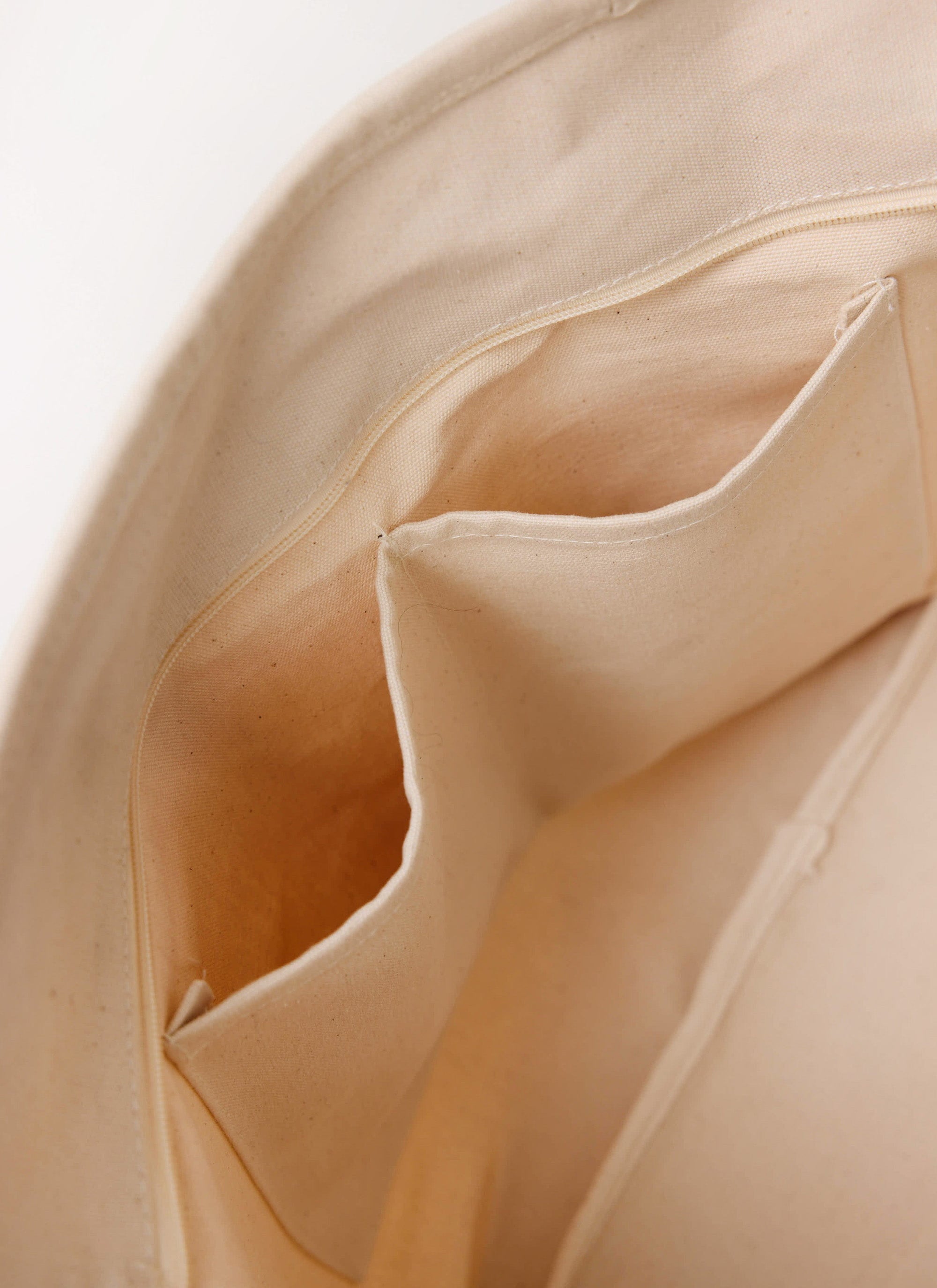 A close-up of the internal zip pocket and compartments inside the ecru cotton Carlo Mixologist Tote Bag from Percival.