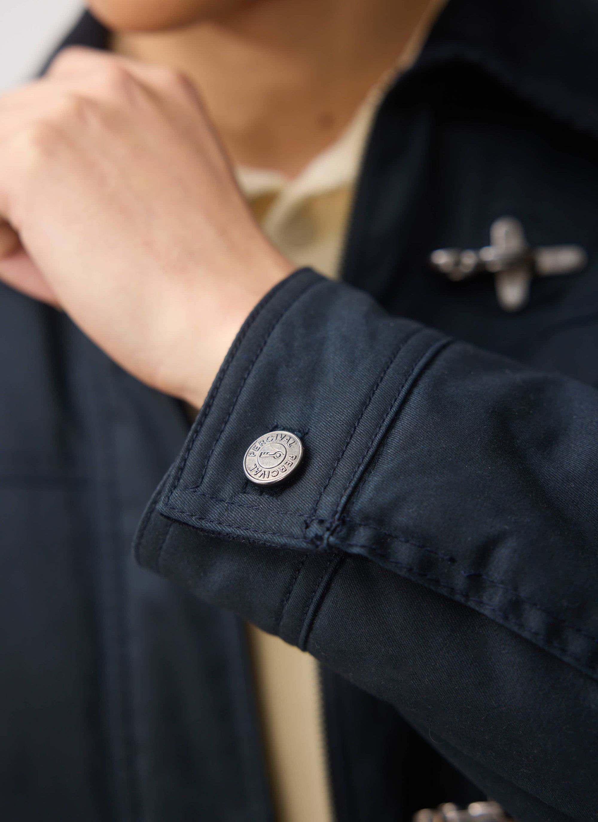 Close up of the cuff of the navy Percival Fontane Wax Jacket, featuring the branded button and metal clasp detail.