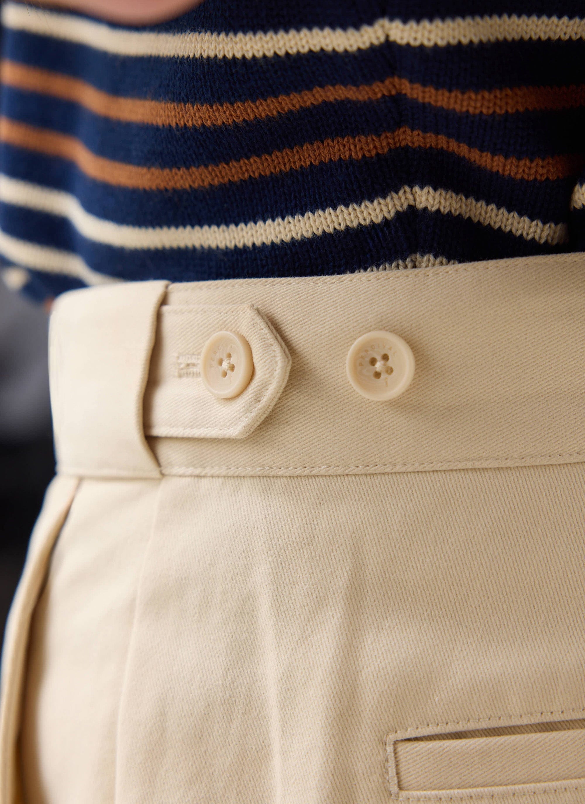 Close up of the button tab waistband on the Percival ecru straight leg chinos, styled with a striped knit top.