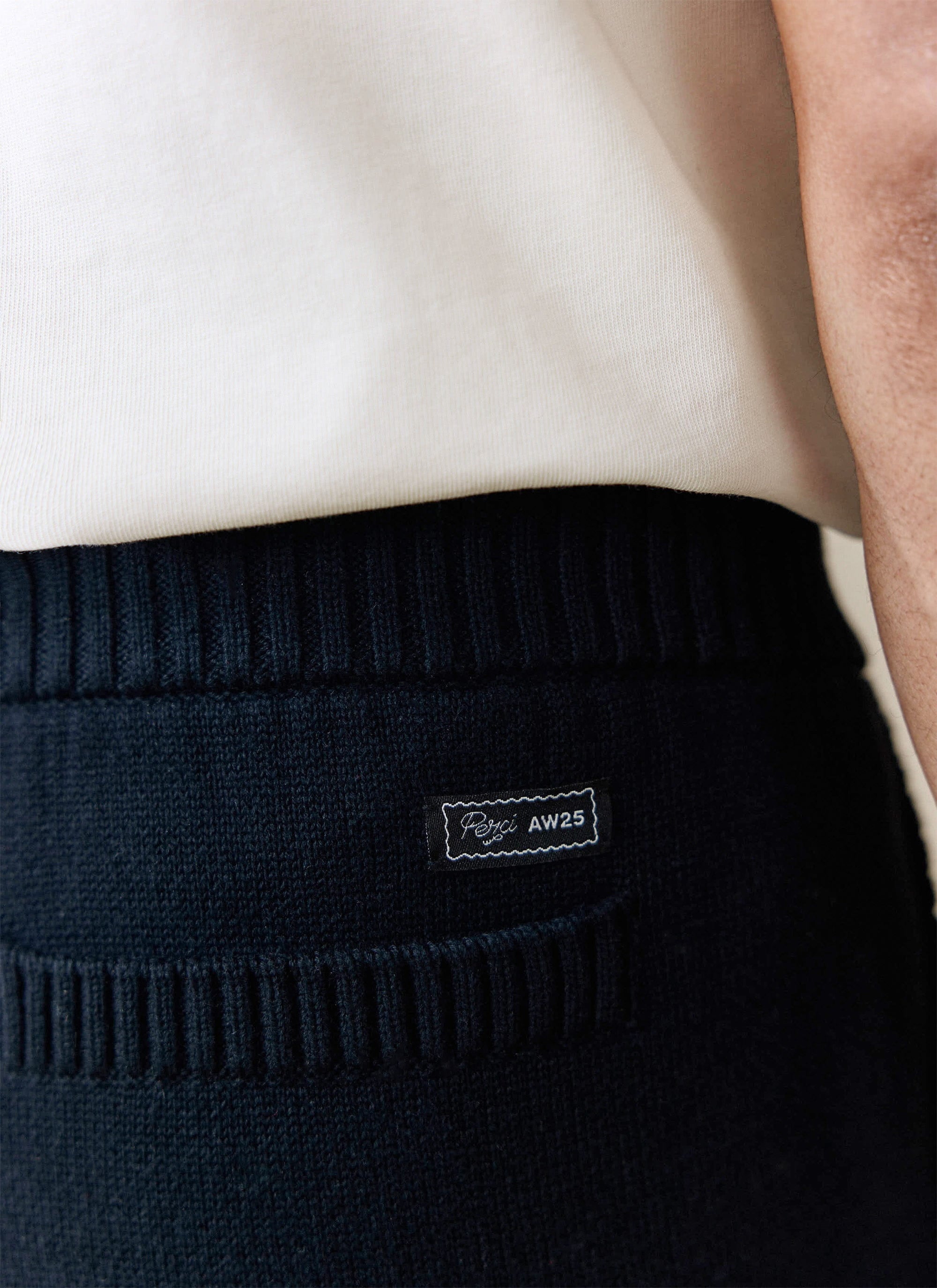 A close-up of the black knitted Chronicle Trackpant from Percival, showing the woven brand label on the back pocket.