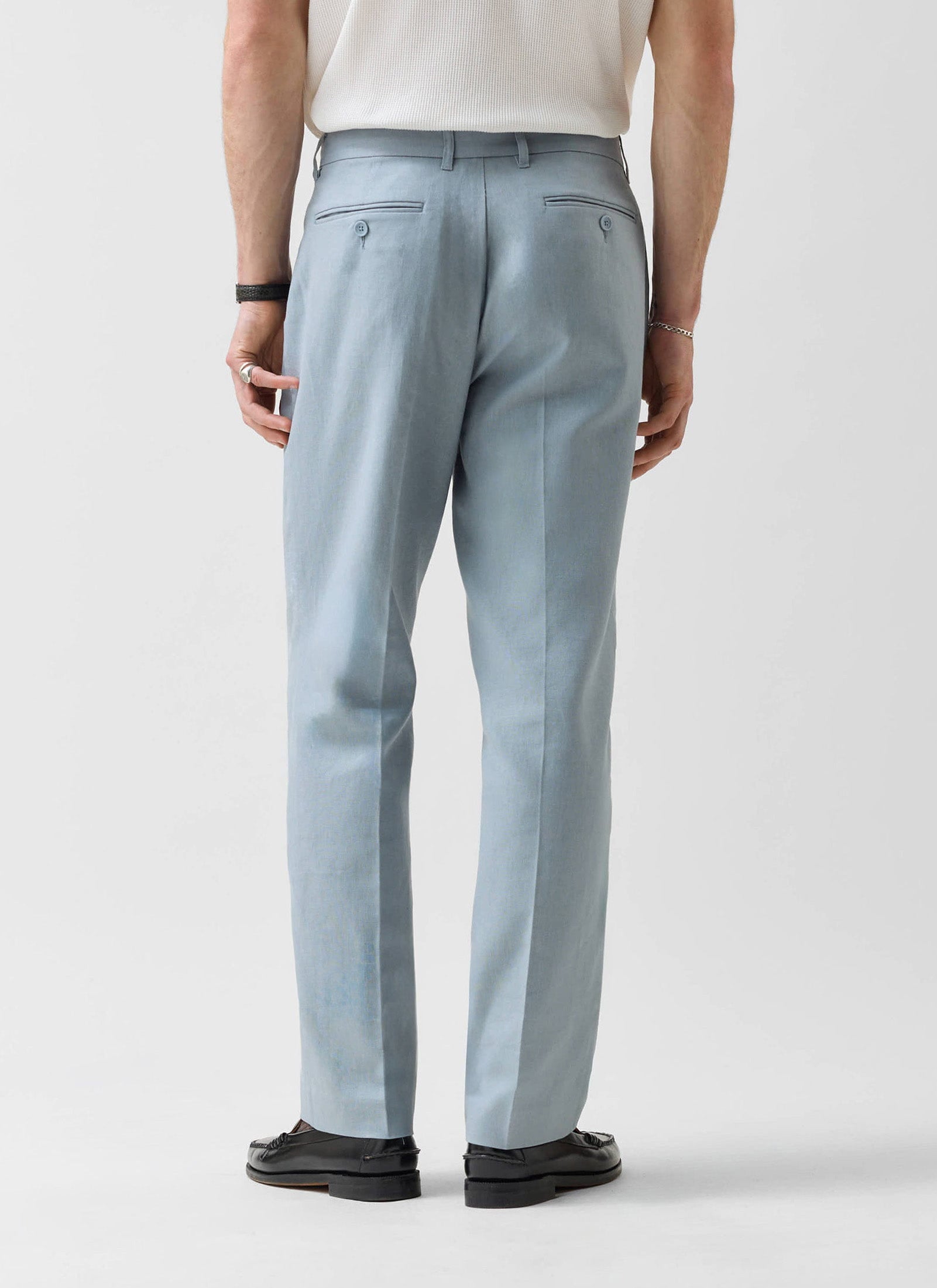 Rear view of a model wearing Percival's light blue tailored linen trousers, showing the straight leg fit and pocket detail.