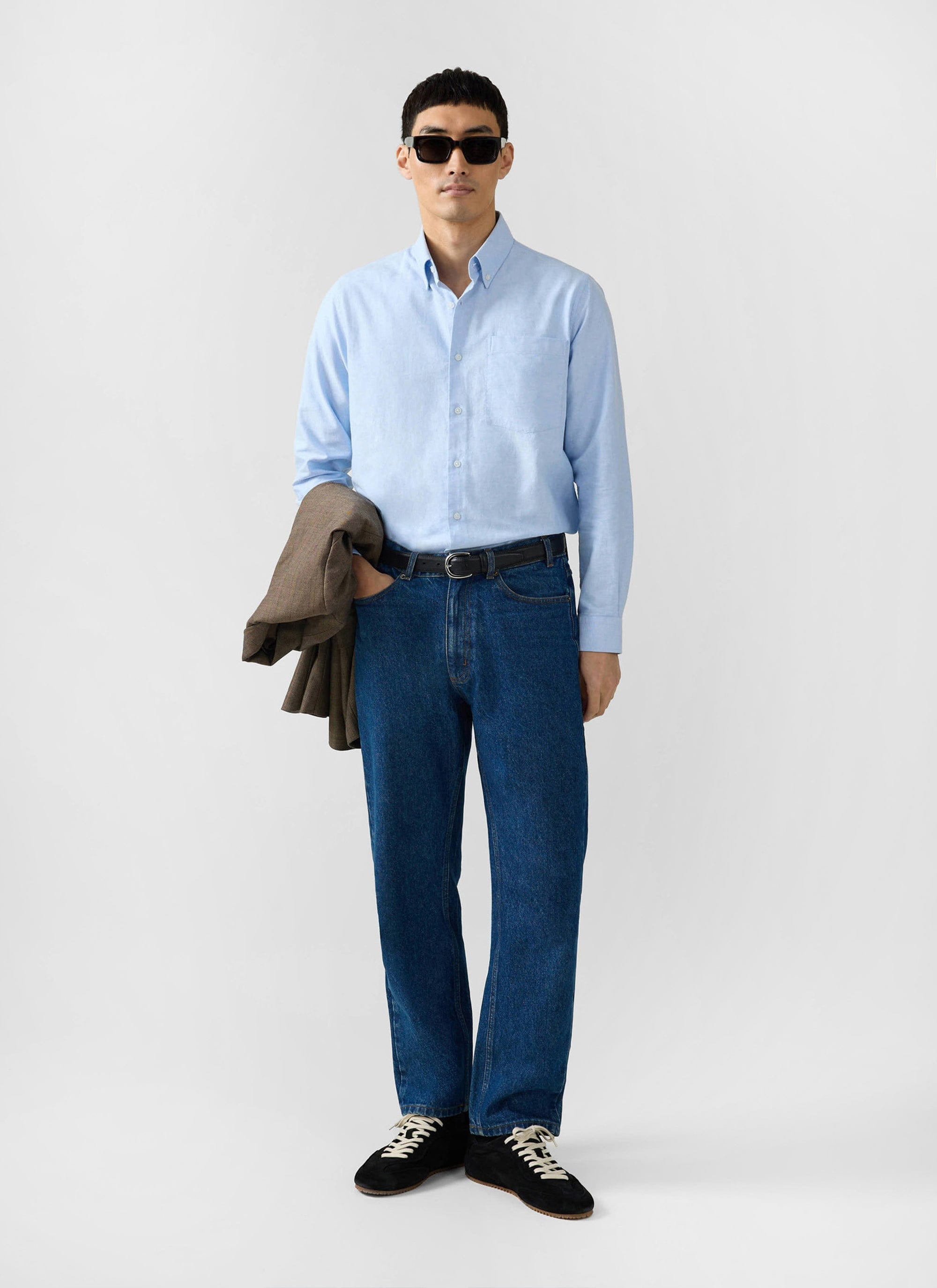 A model wears the Percival Oxford Regular Shirt in light blue, styled with dark denim jeans and sunglasses.