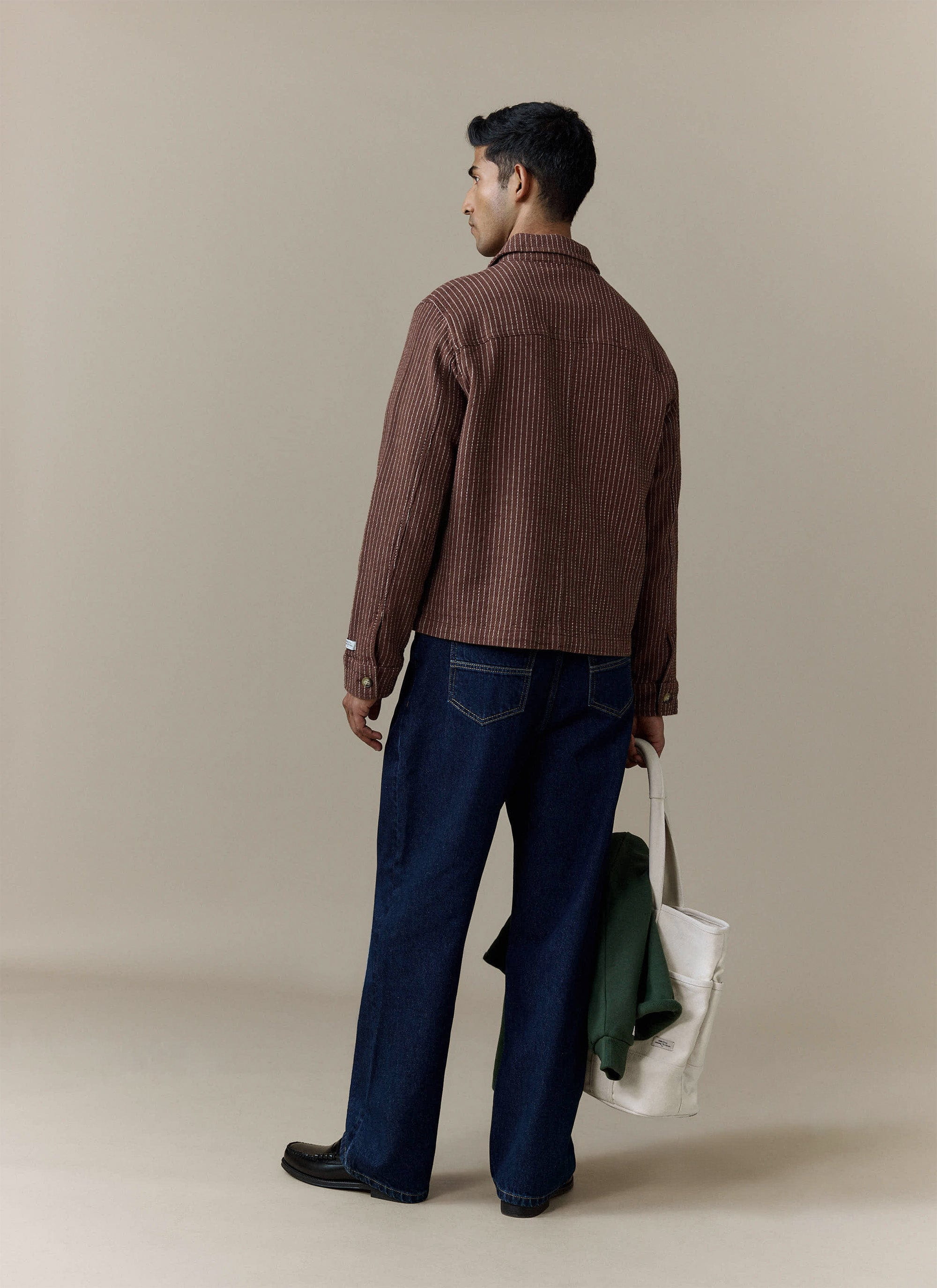 Back view of a model wearing the Percival Sorrento Boxy Overshirt in brown linen, styled with wide-leg jeans and a tote bag.