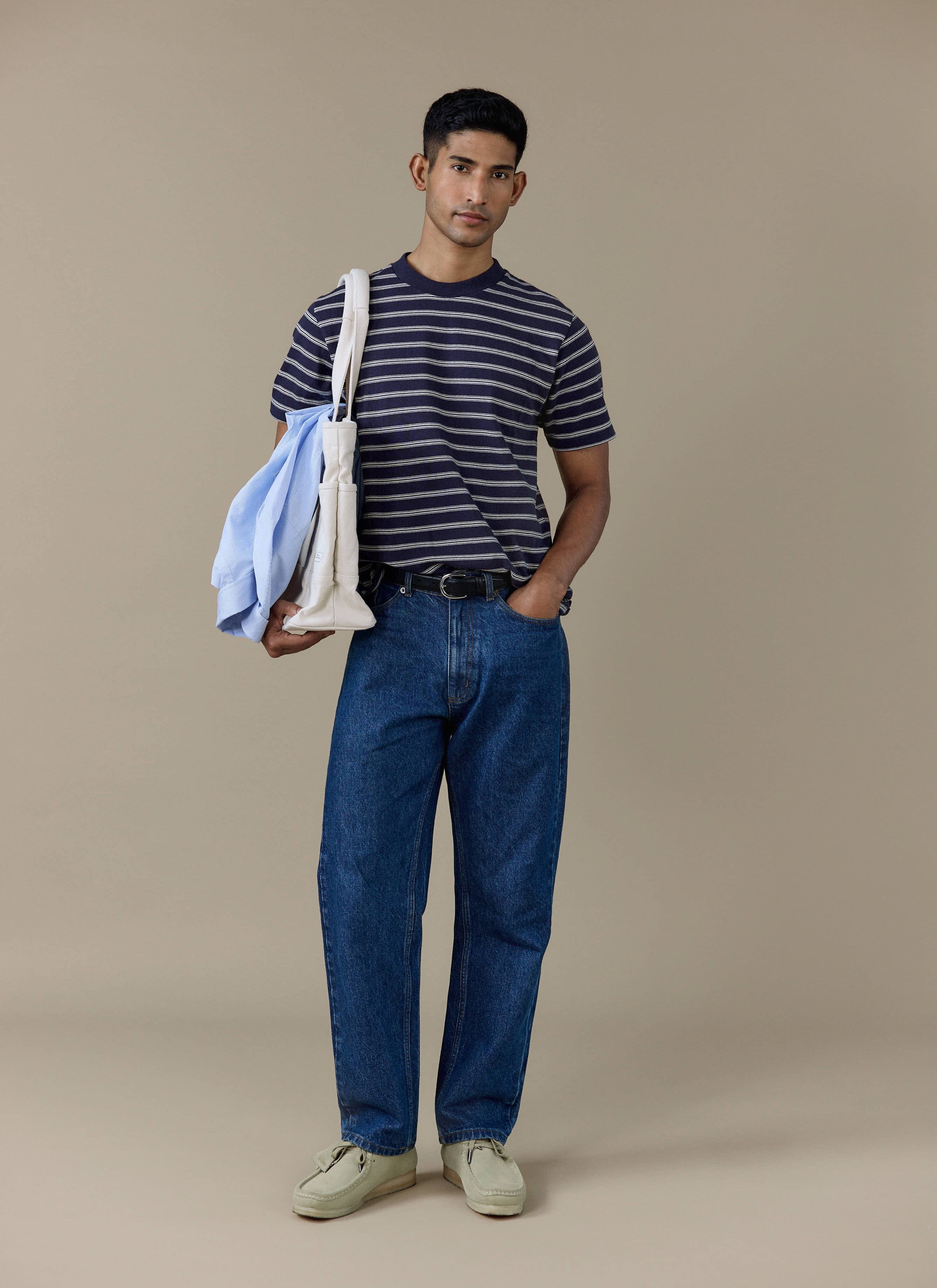 Model wearing the Percival Arlo Raw Hem Breton T Shirt in navy stripe, styled with blue jeans and a white tote bag.