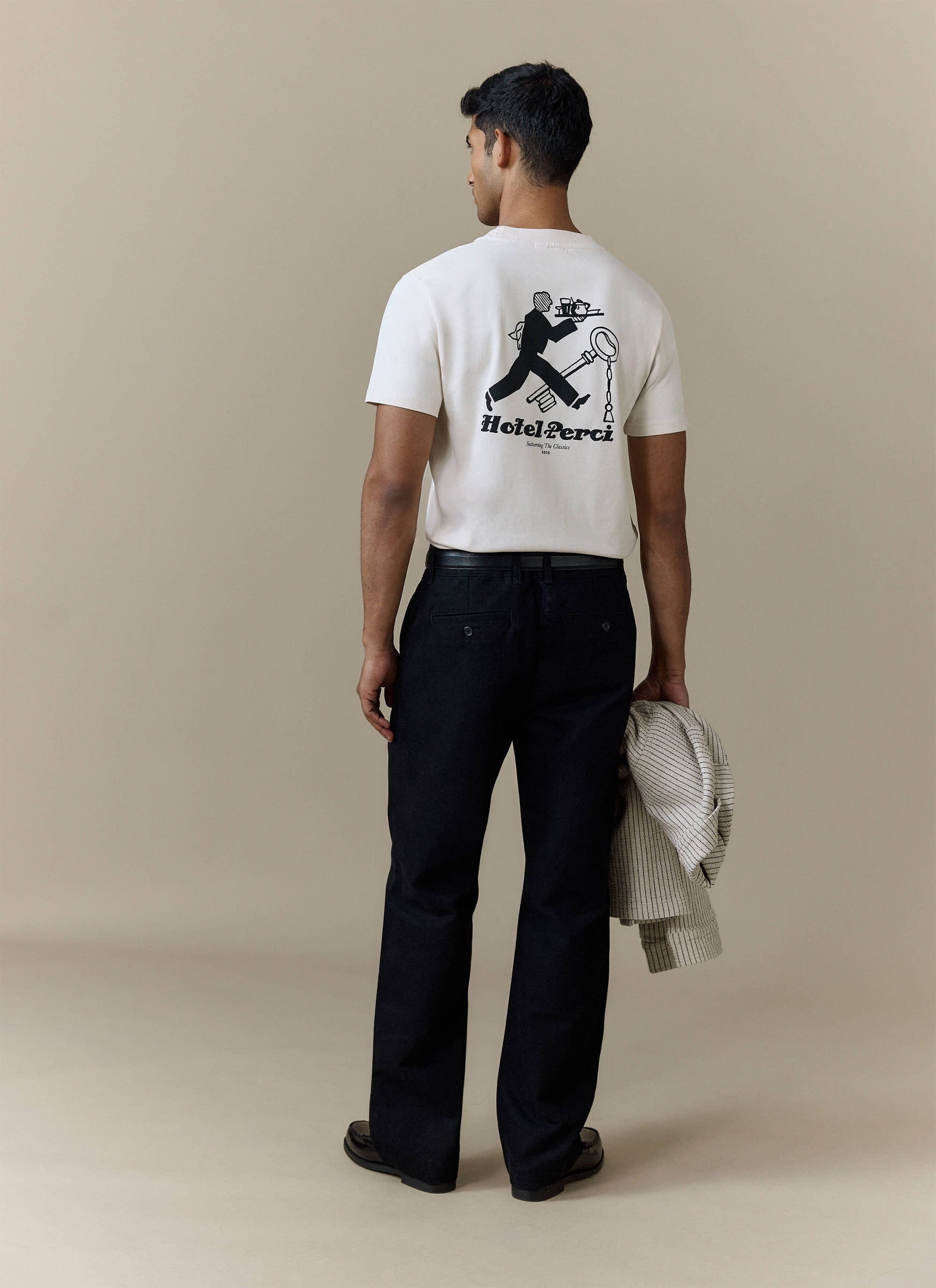 Back view of a model wearing the ecru Hotel T Shirt from Percival, showing the illustrated 'Hotel Perci' graphic.