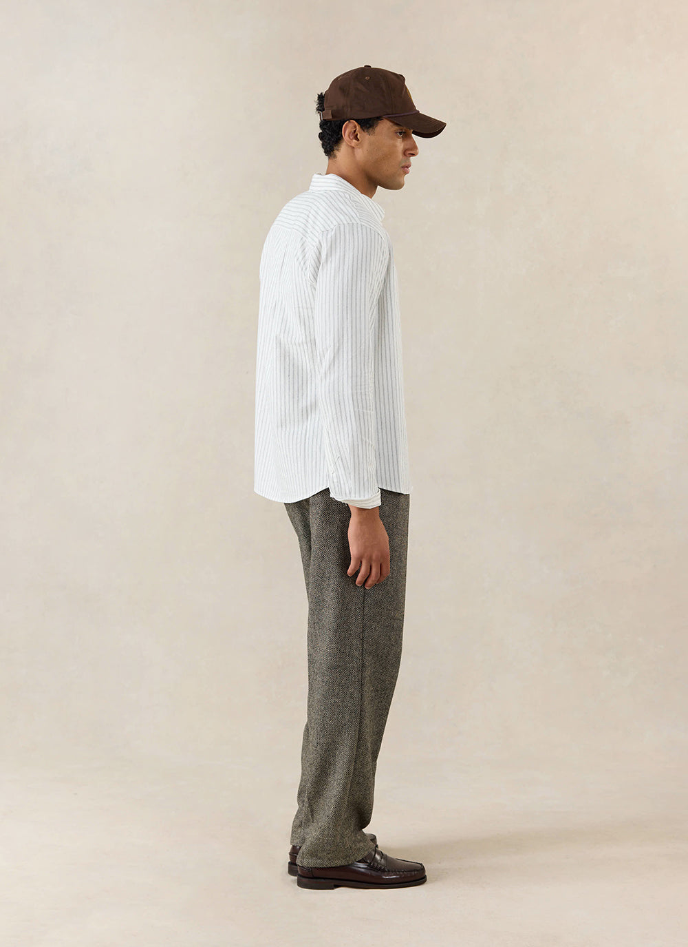 A model wears the white cotton Fabian Striped Shirt from Percival, styled with textured trousers and a brown cap.