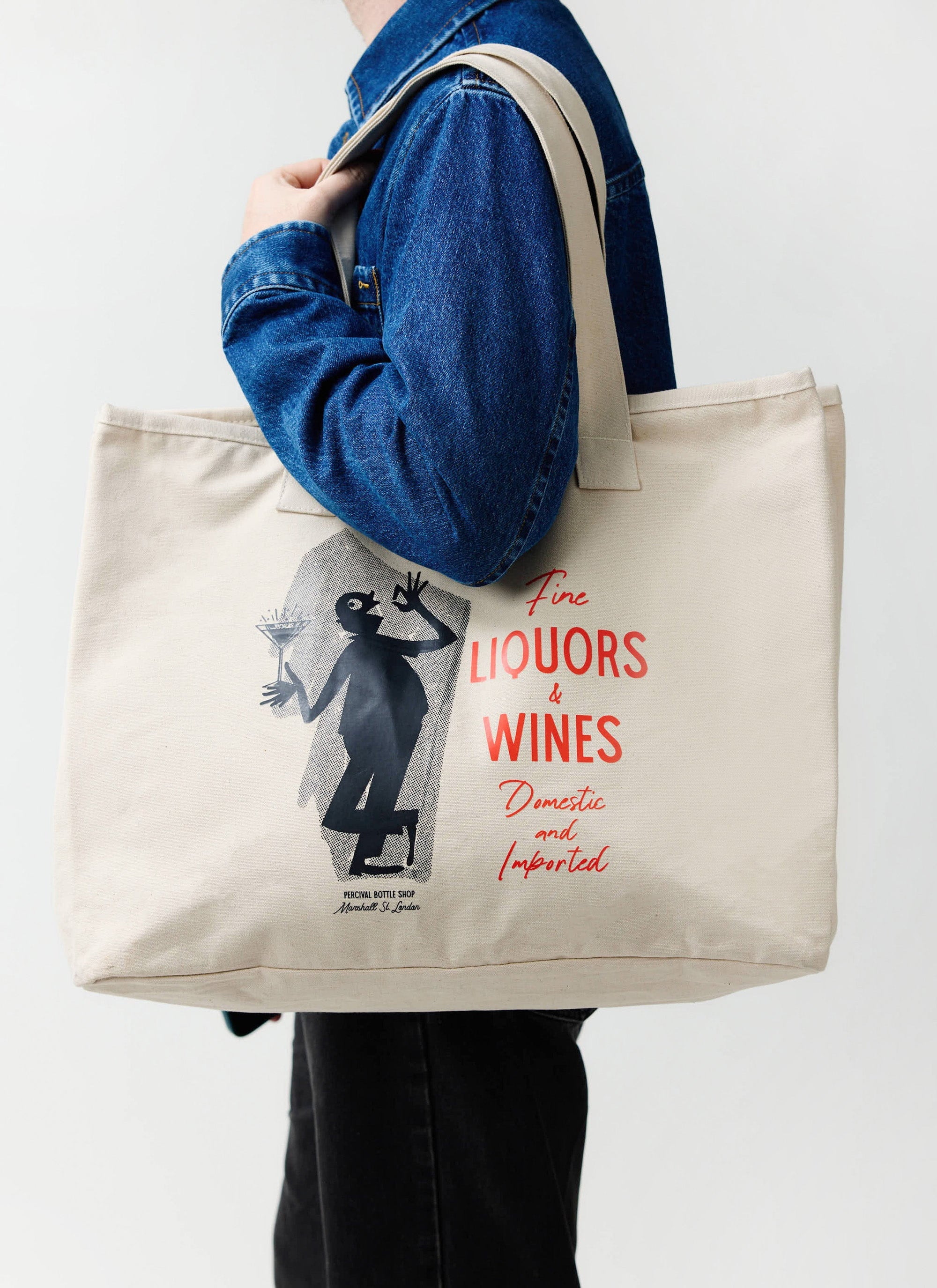A model wears the Percival Carlo Mixologist tote bag in ecru, carried over the shoulder of a blue denim jacket.