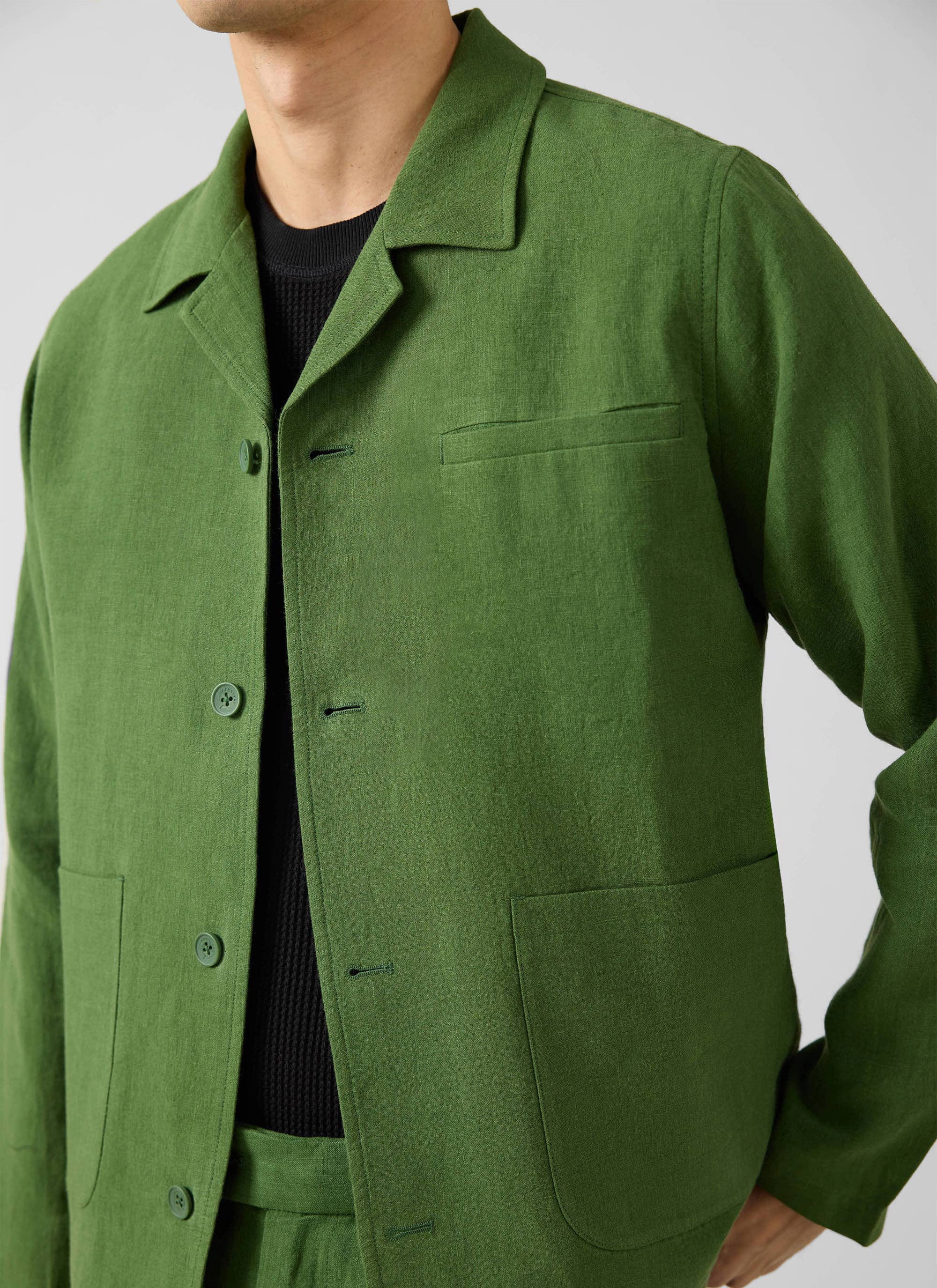 Close-up of a model wearing the Percival Linen Overshirt in forest green over a black knitted top.