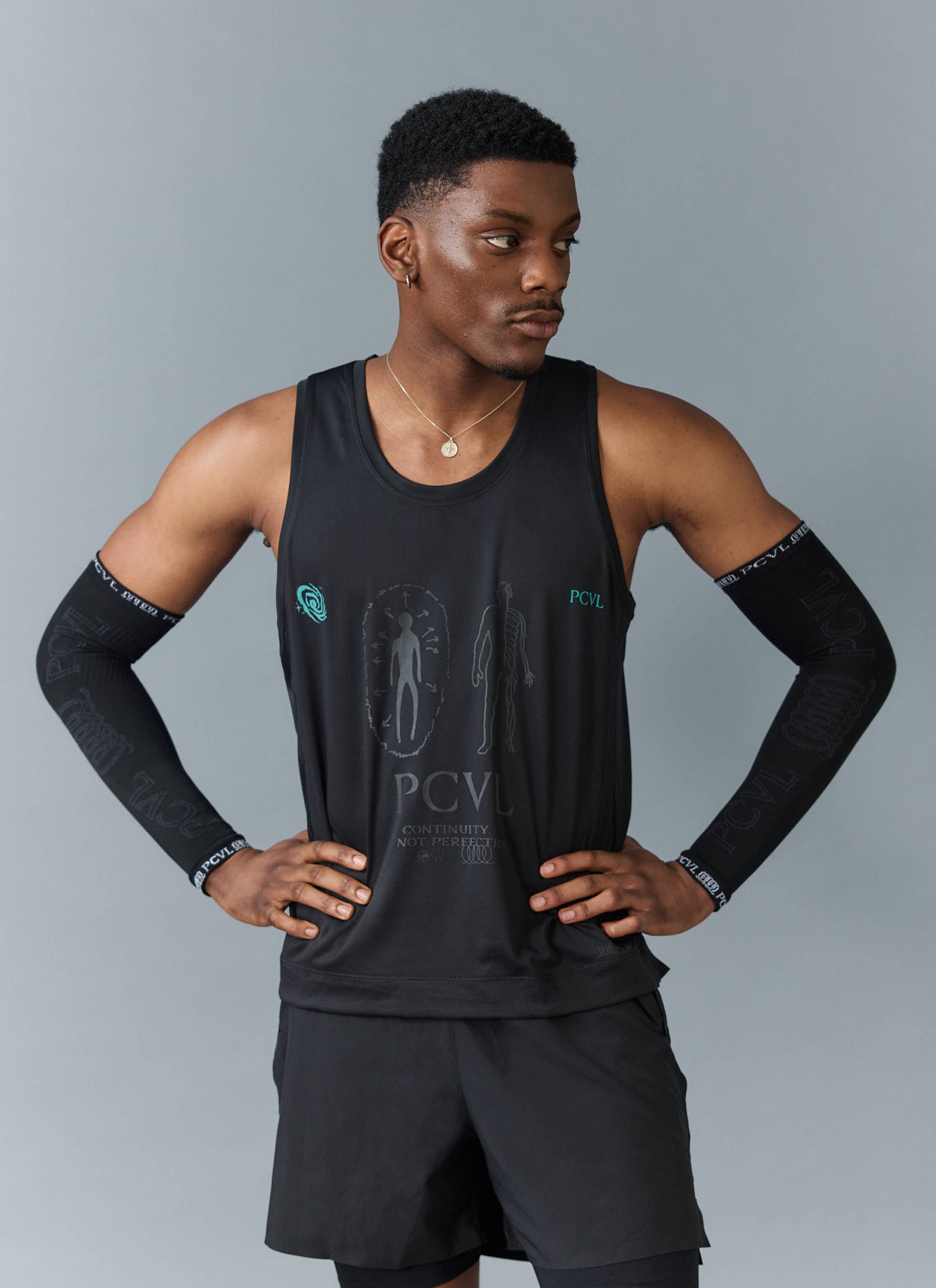 A model wears the Percival PCVL Arm Compression sleeves in black with an athletic vest, posing with hands on hips.
