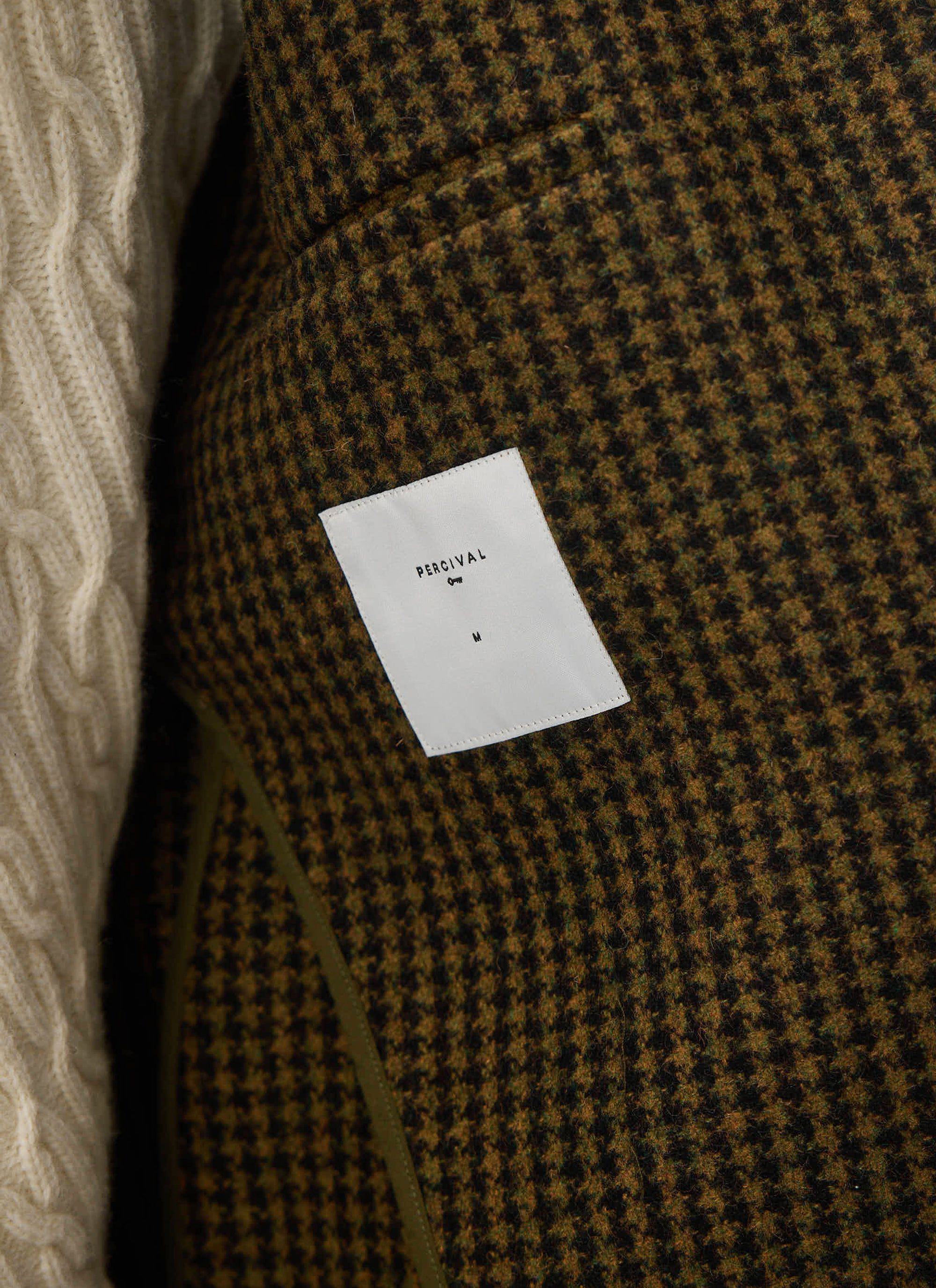 A close-up of the inner label of the Percival Dickens Car Coat, showcasing the brown Watcher Check houndstooth wool fabric.