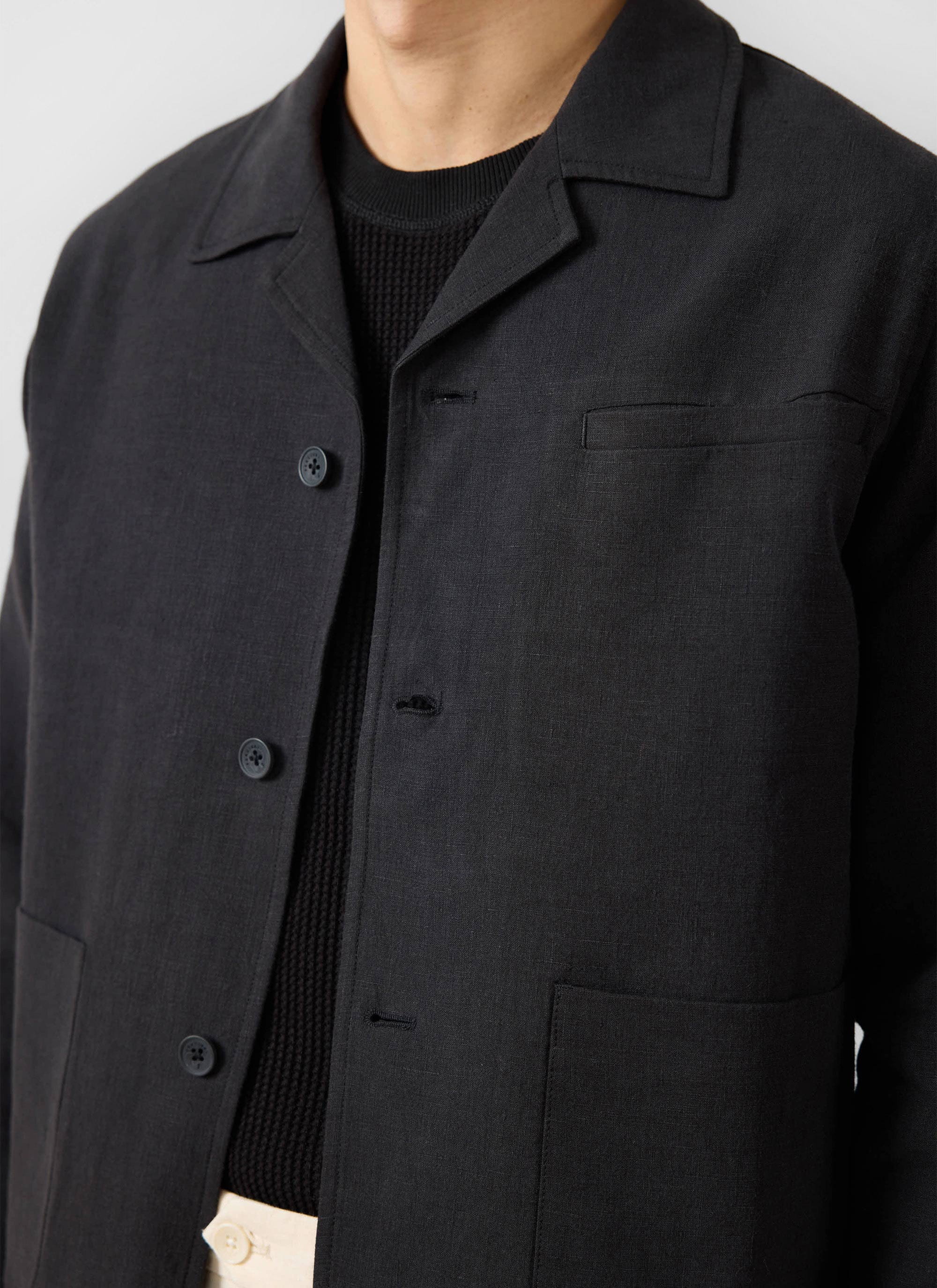 A close-up of a model wearing the Percival black linen overshirt, showing the collar and chest pocket detail.