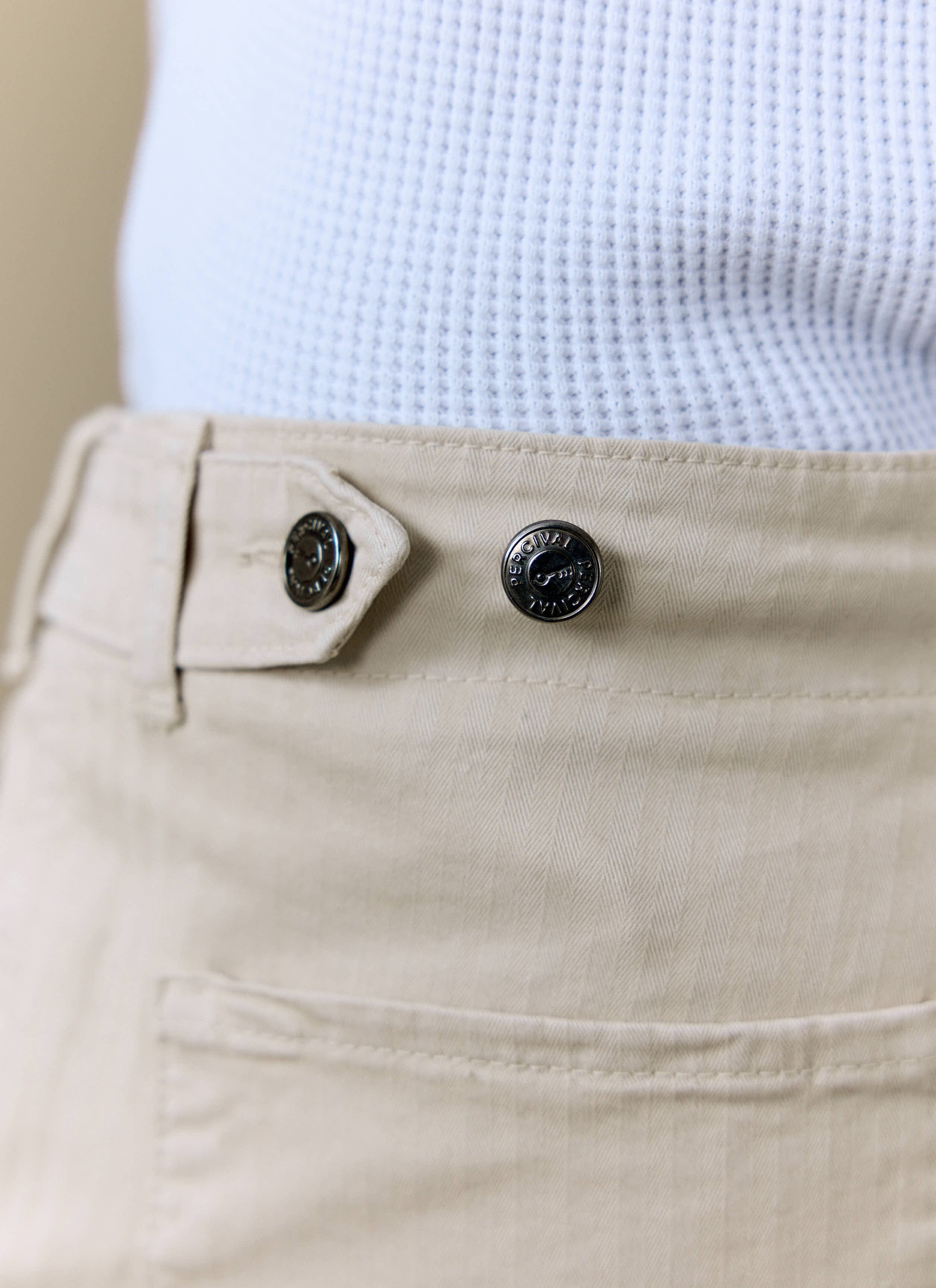 Detail of the Percival Lungo Herringbone Straight Trousers in cream, showing the branded waist buttons and fabric texture.