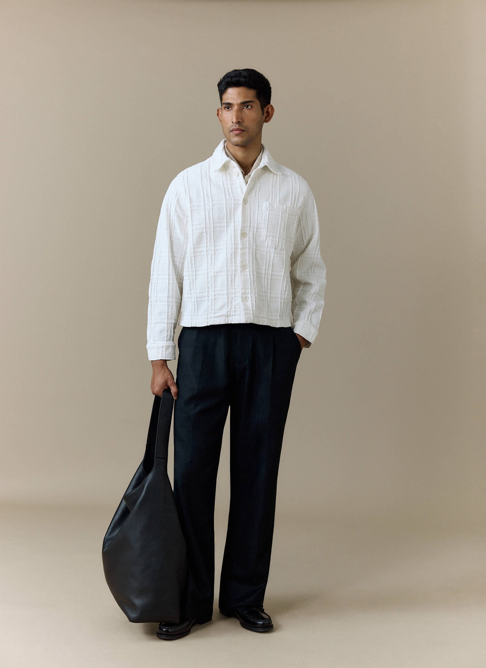 A model wears the Percival Canyon Heavyweight Overshirt in ecru, styled with black trousers and holding a black bag.