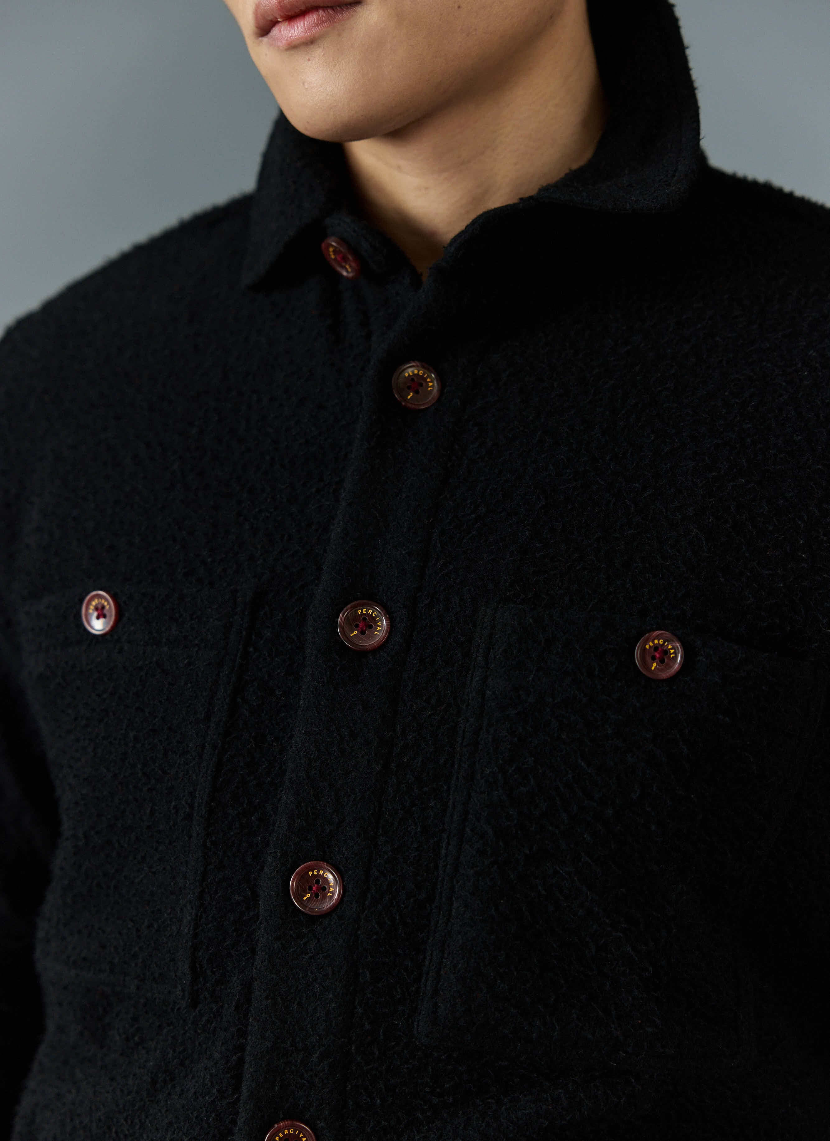 A close-up of the Percival Blanket Overshirt in black Casentino wool, showing the textured fabric and branded buttons.