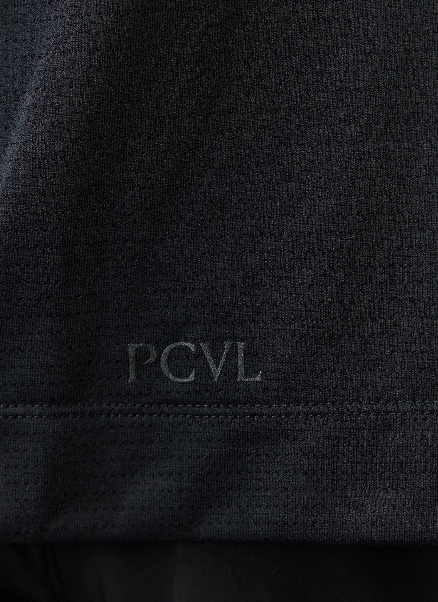 A close-up of the tonal PCVL logo on the black recycled technical jersey of the Percival Performance Vest.