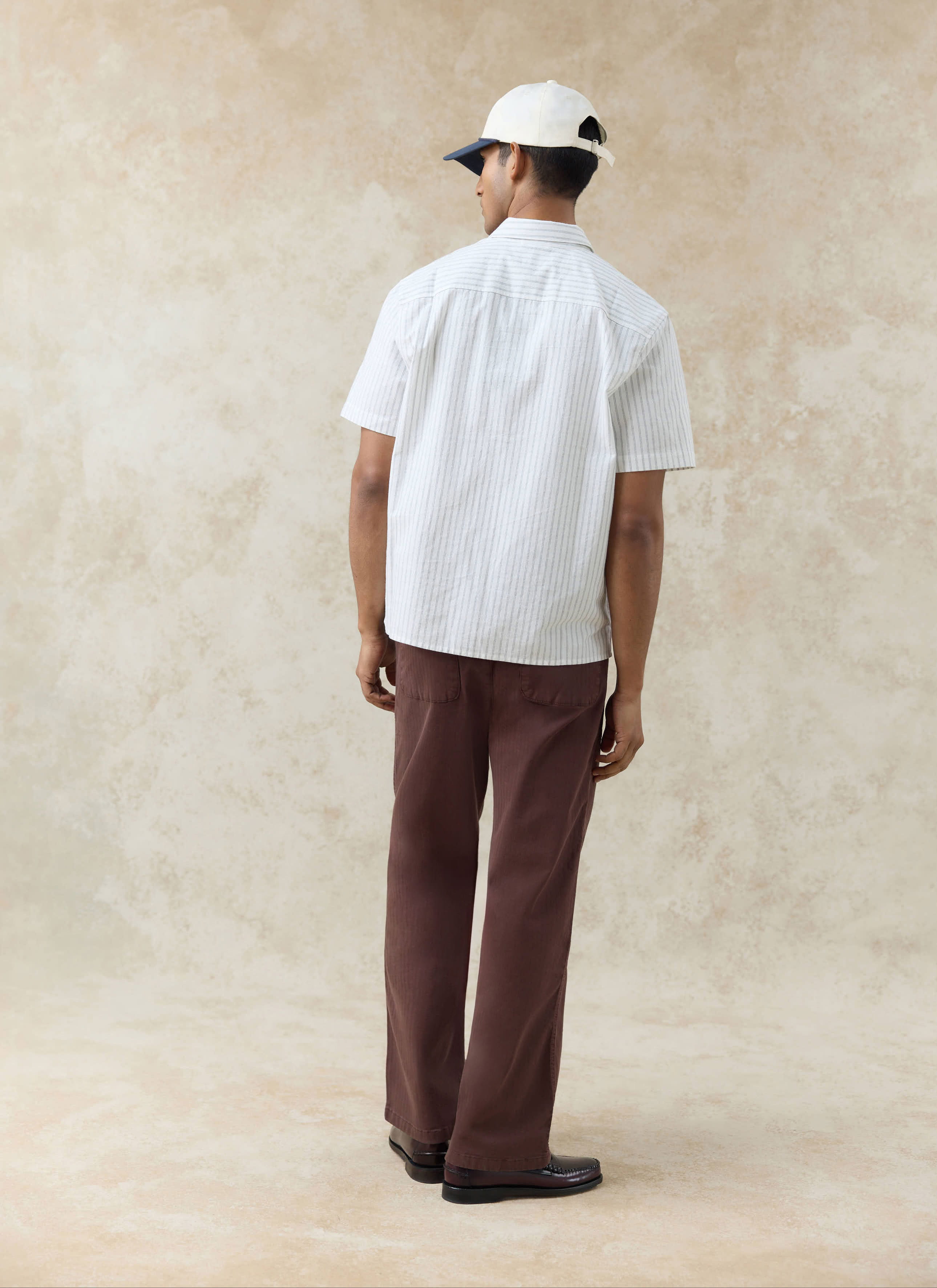 The back of a model wearing the Percival Lucia Embroidered Shirt in cream stripe cotton, styled with brown trousers.