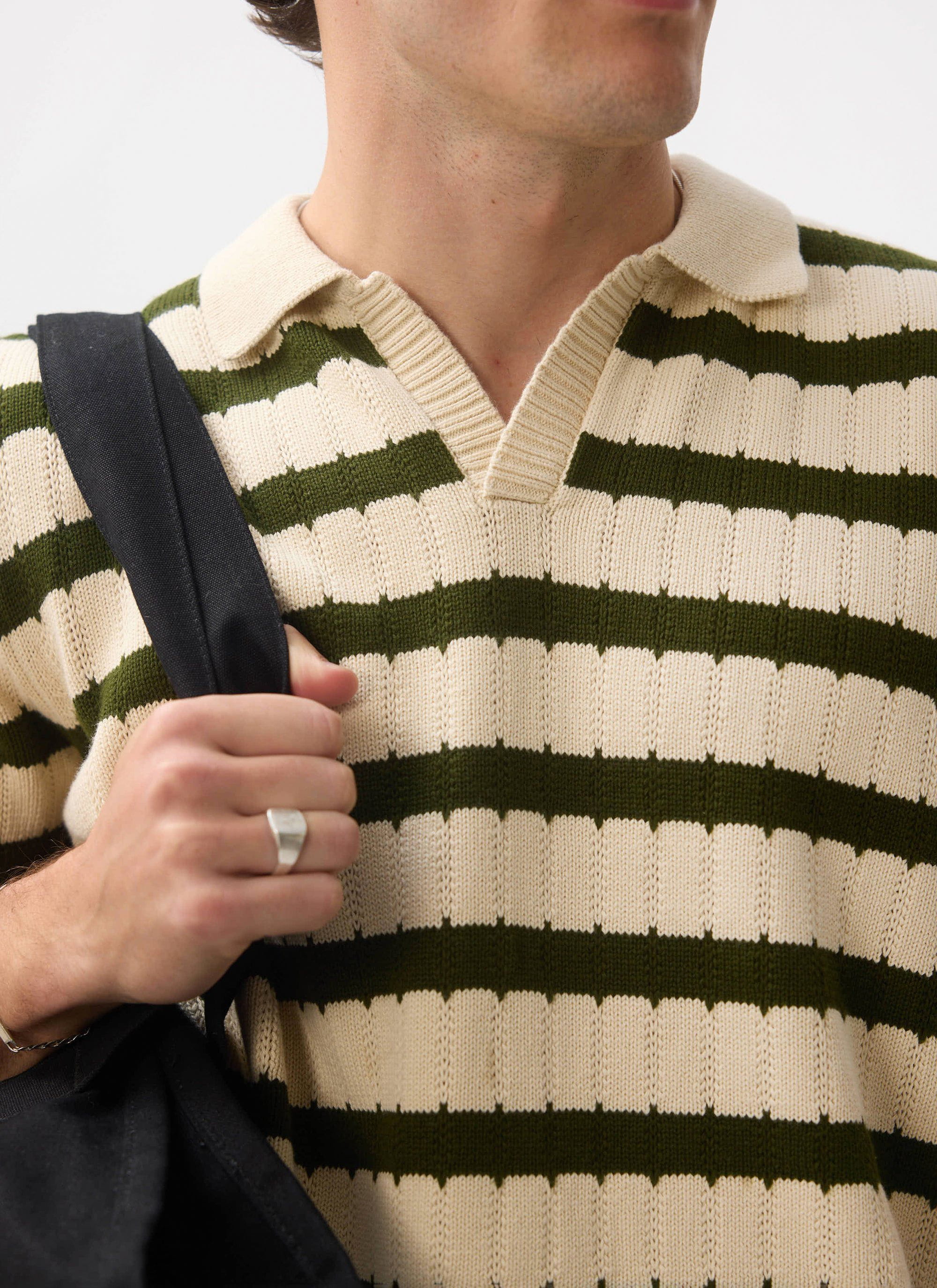 A close-up of a model wearing the Percival Stine Knitted Polo in ecru, showing the green striped jacquard knit.