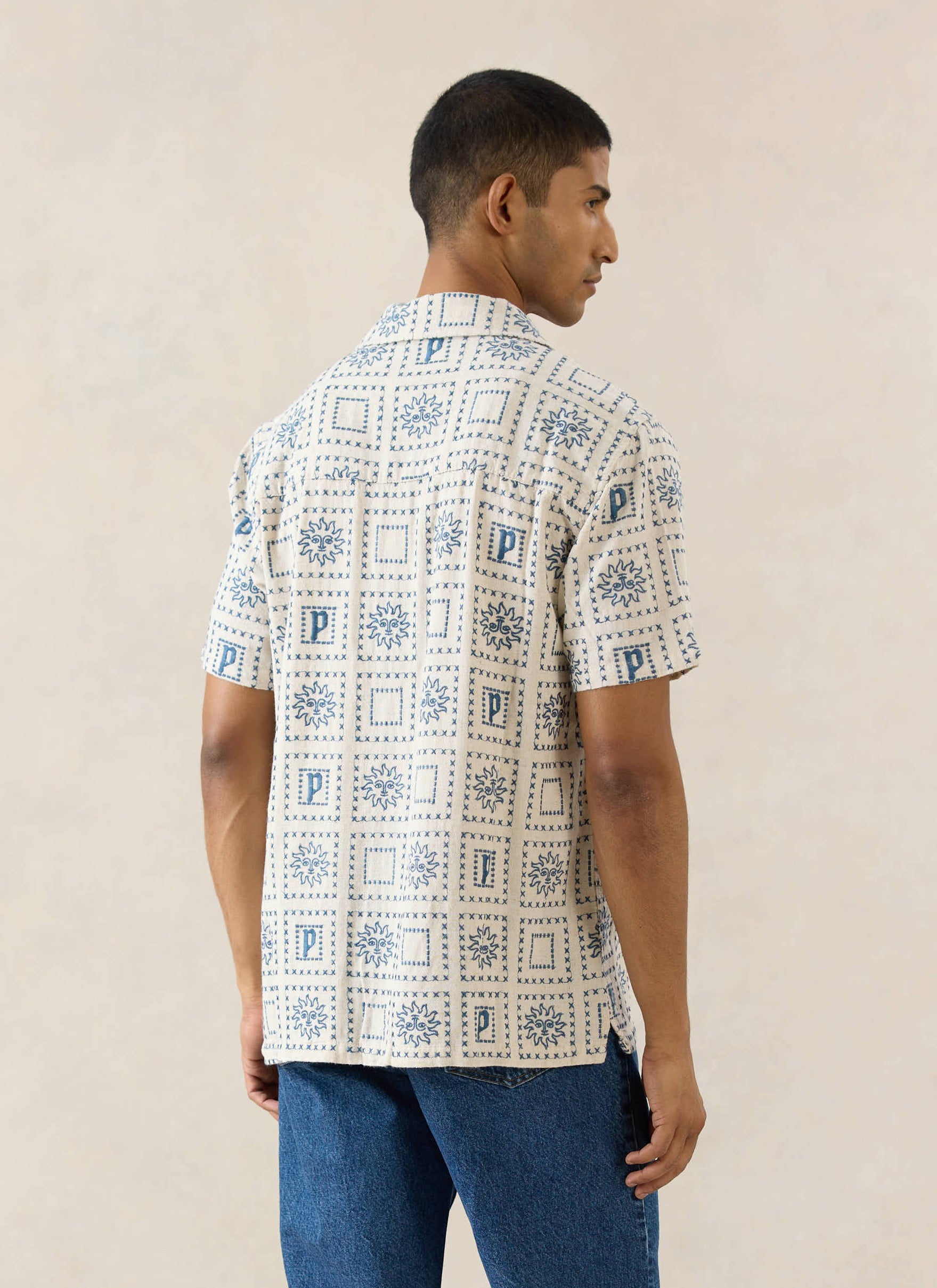 The Percival Solis Heaton Cuban Shirt in cream linen blend, featuring blue embroidered sun motifs, shown from the back.