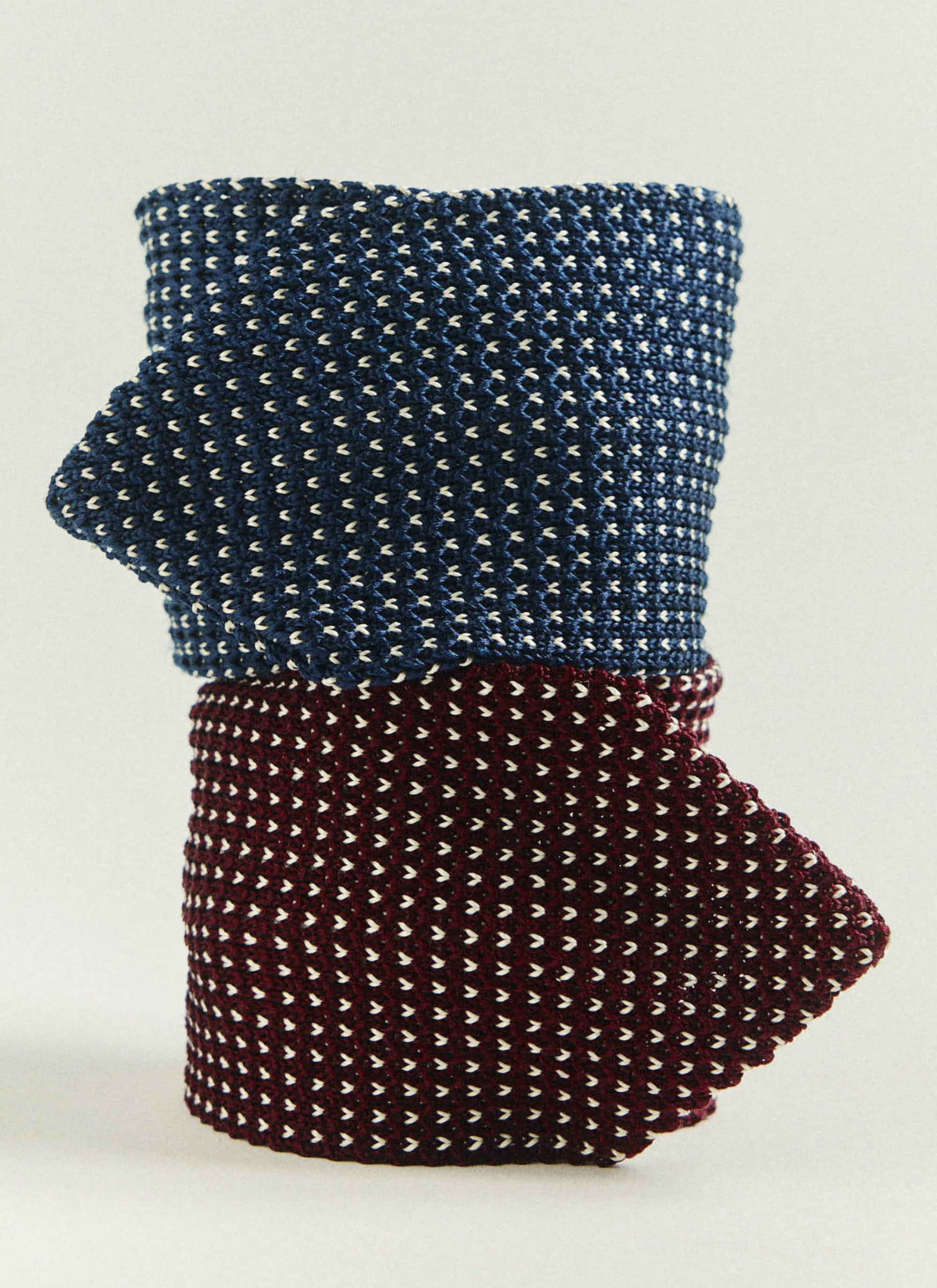 The Percival Birdseye Silk Tie in blue and burgundy, rolled and stacked to display the intricate birdseye knit.