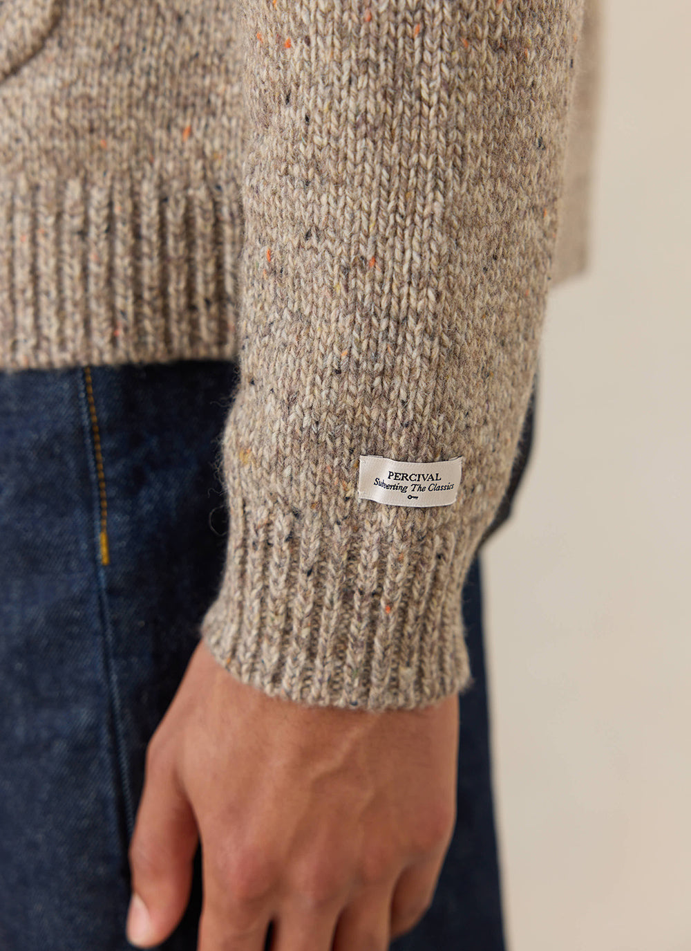 Close-up of the oak Percival Rhodes Cardigan, showing the textured knit and branded label on the ribbed cuff.