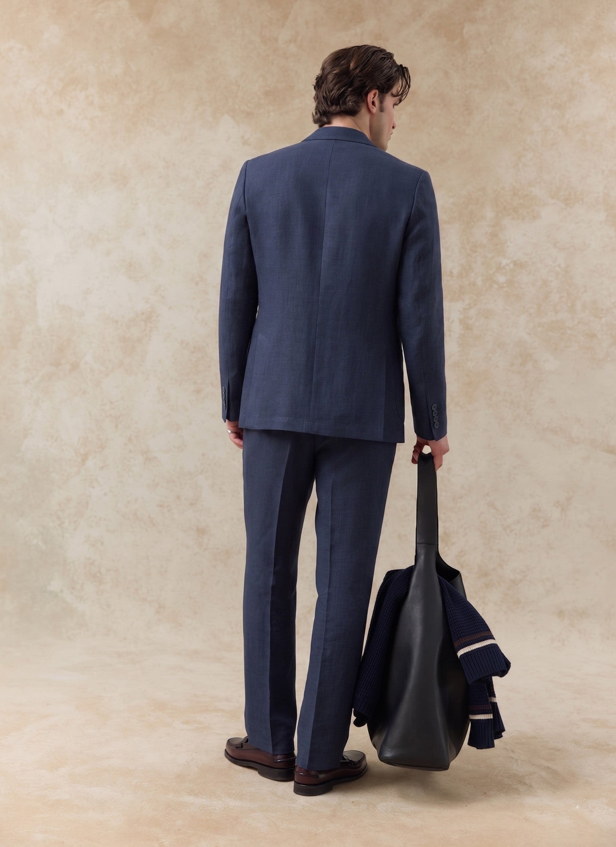 Rear view of the Percival navy tailored linen trousers and matching suit blazer, styled with a black leather bag.