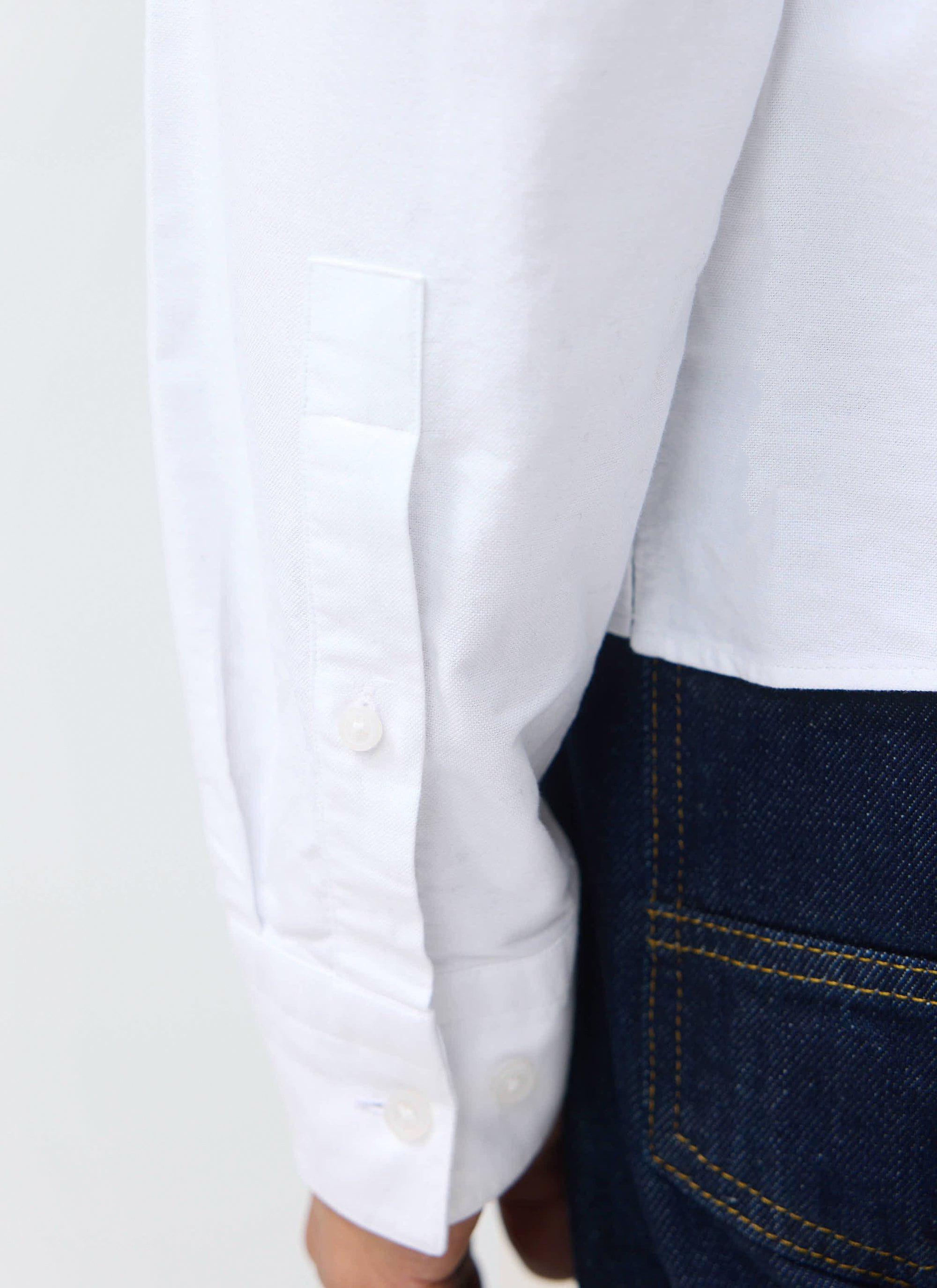 A close-up of the cuff and sleeve detail of the white Guinness x Percival Button Down Boxy Shirt, worn with dark denim.