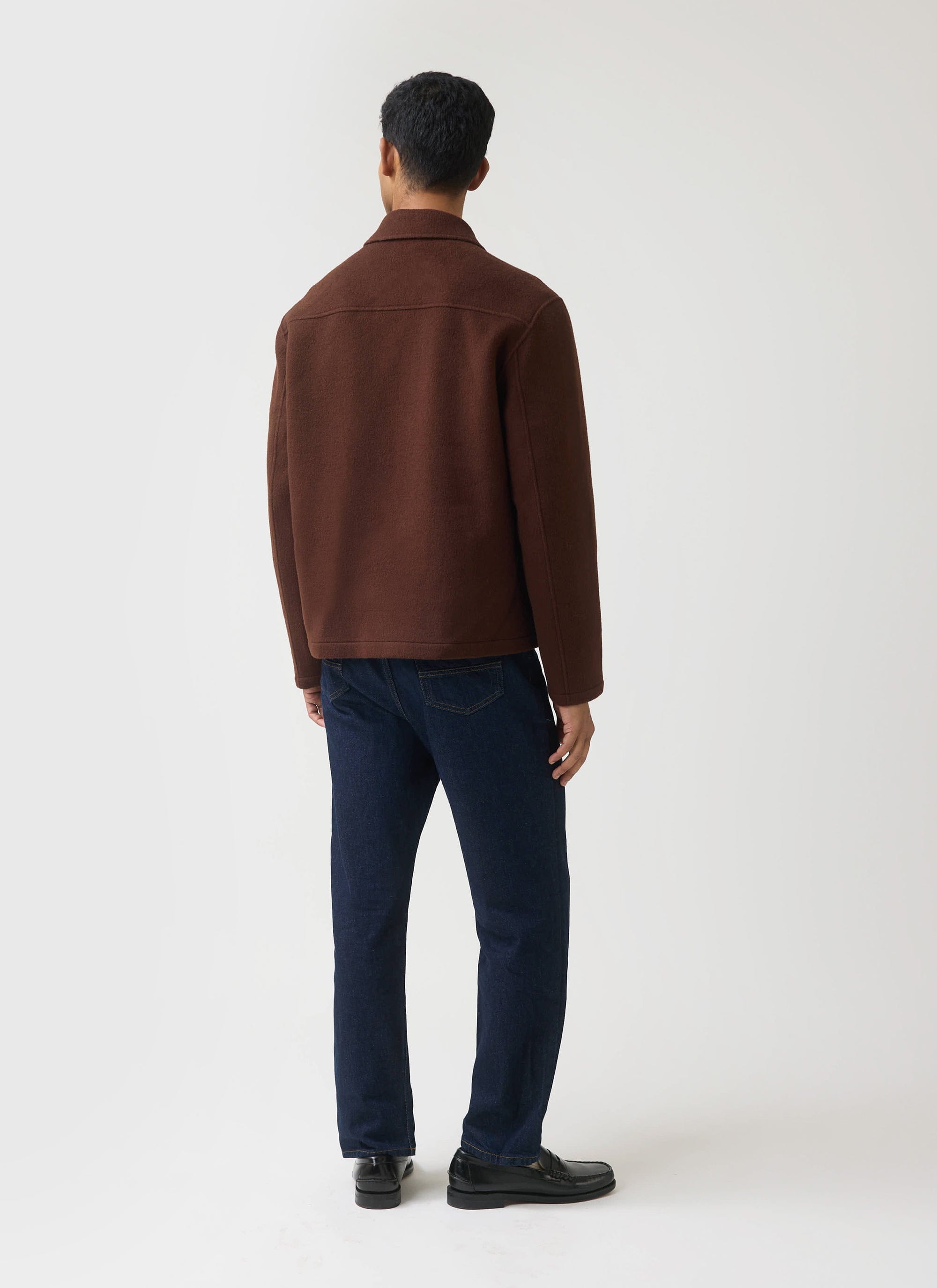 The back of a model wearing the Percival x Guinness Wool Jacket in espresso brown, styled with dark denim.