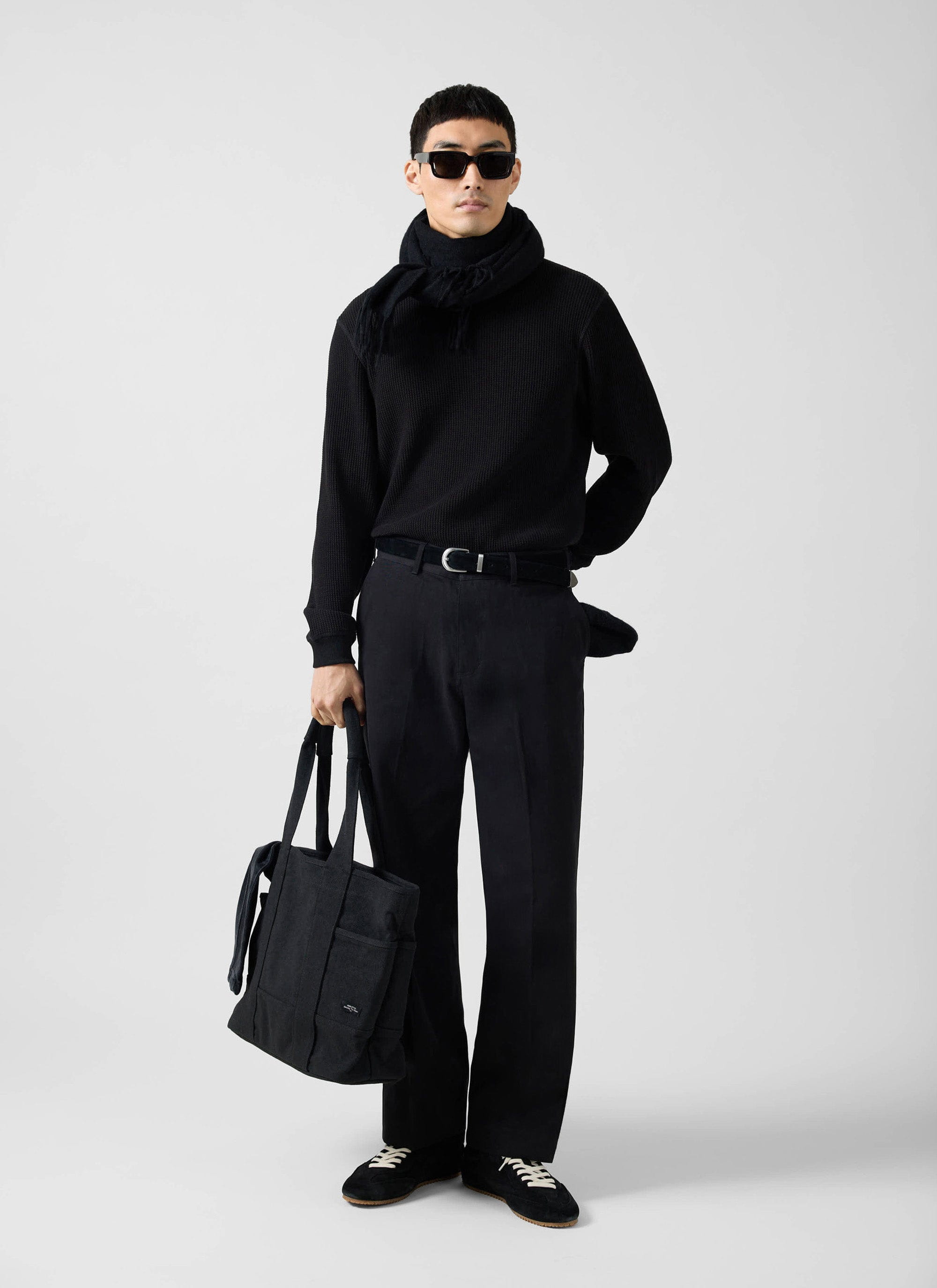 A model wears the black Waffle Long Sleeve T-Shirt from Percival, styled with black trousers, a scarf and sunglasses.