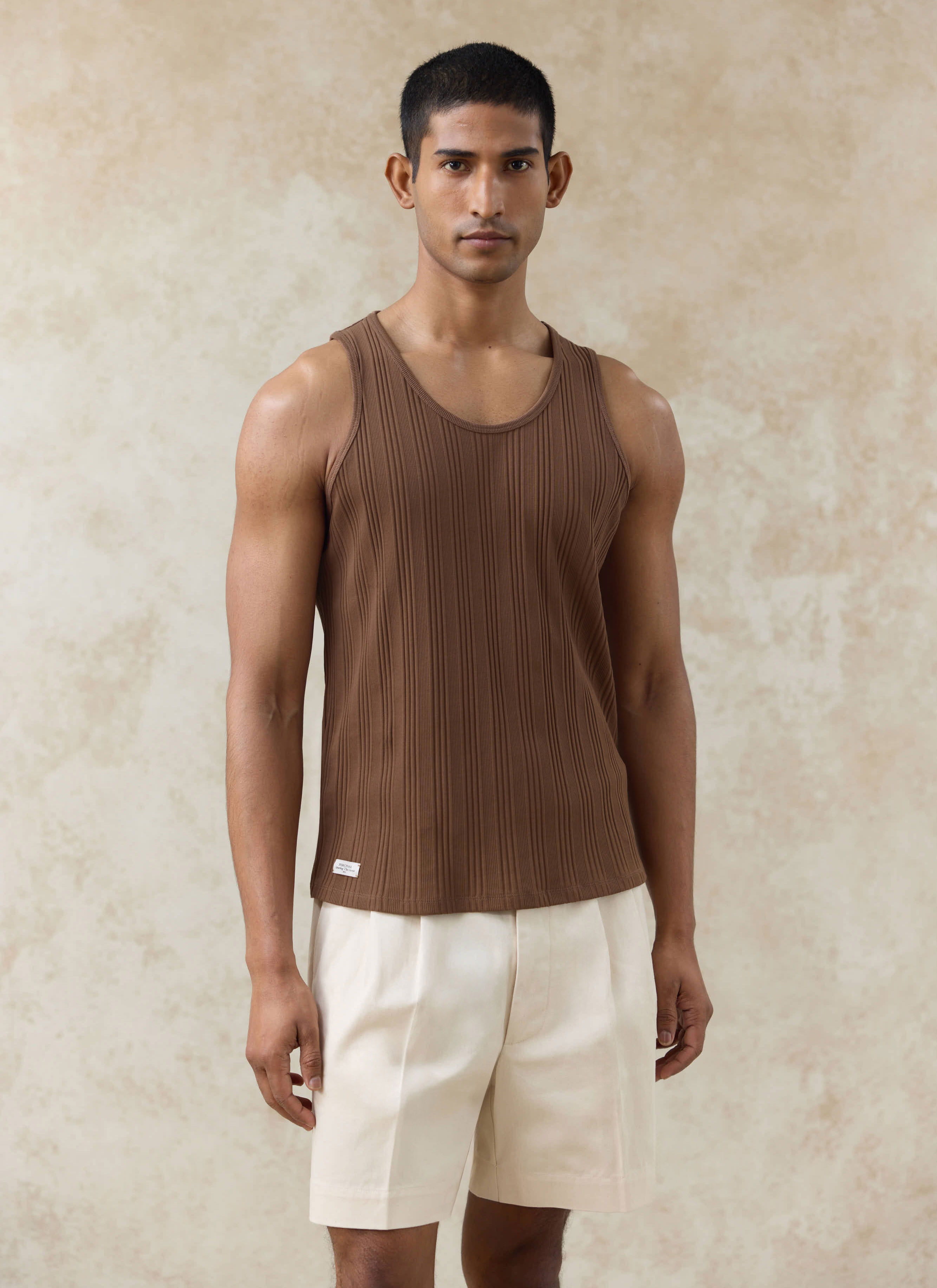Brown Leon Ribbed Vest by Percival in organic cotton, styled on a model with cream pleated shorts.