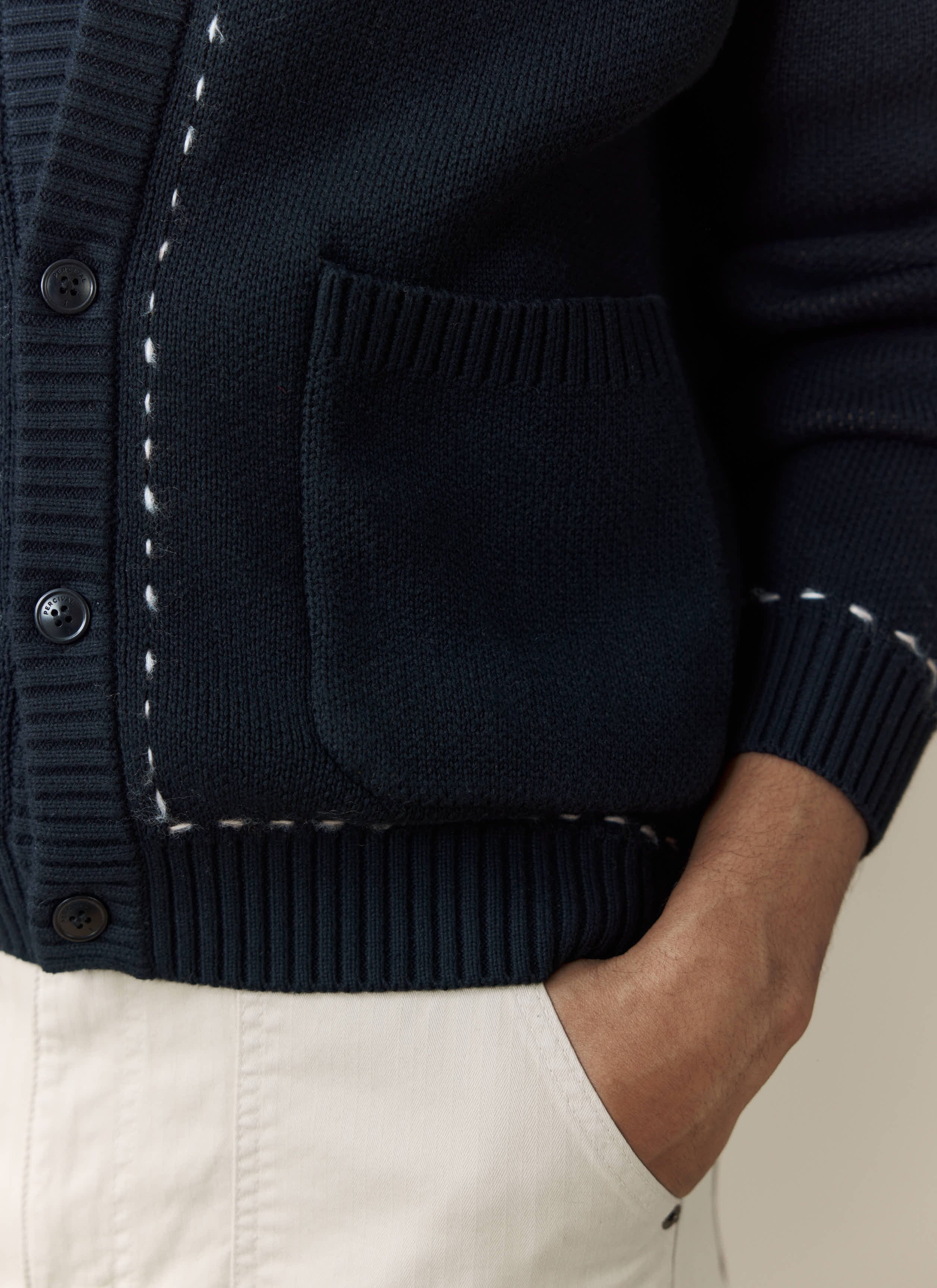 Close-up detail of the Percival Module Boxy Cardigan in black, showing the pocket, branded button and contrast stitching.
