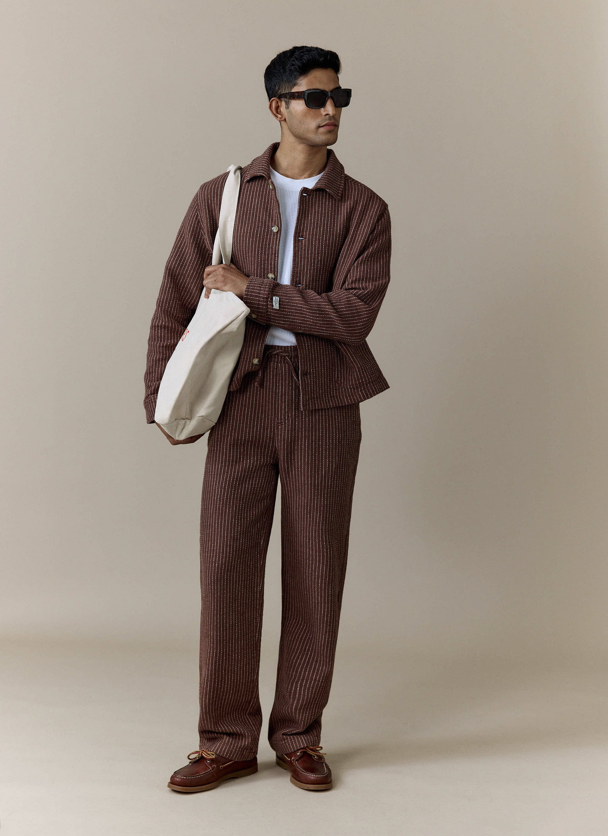 A full-length shot of a model wearing the Percival Sorrento Boxy Overshirt and matching trousers in a brown striped linen.