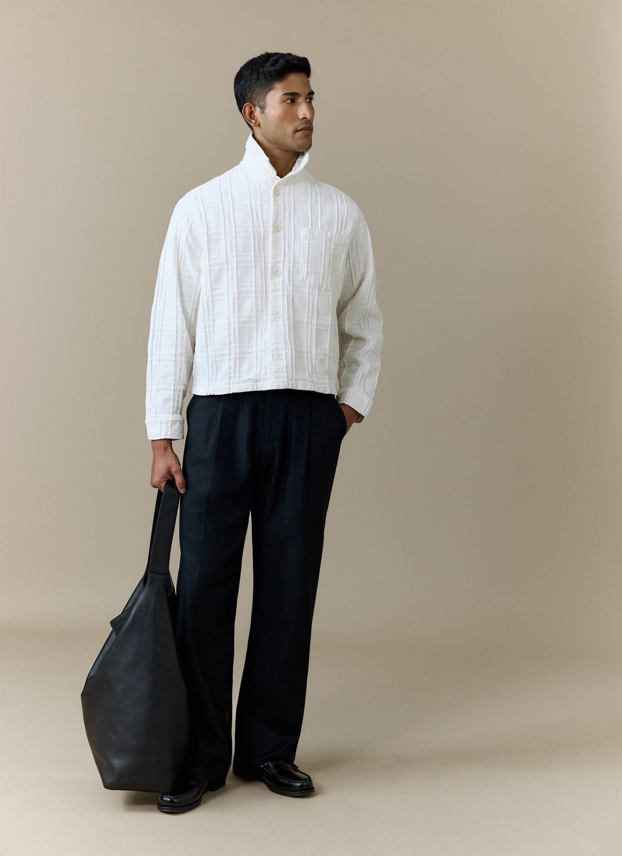 A model wears the ecru Canyon Heavyweight Overshirt from Percival, styled with black trousers and holding a black tote bag.