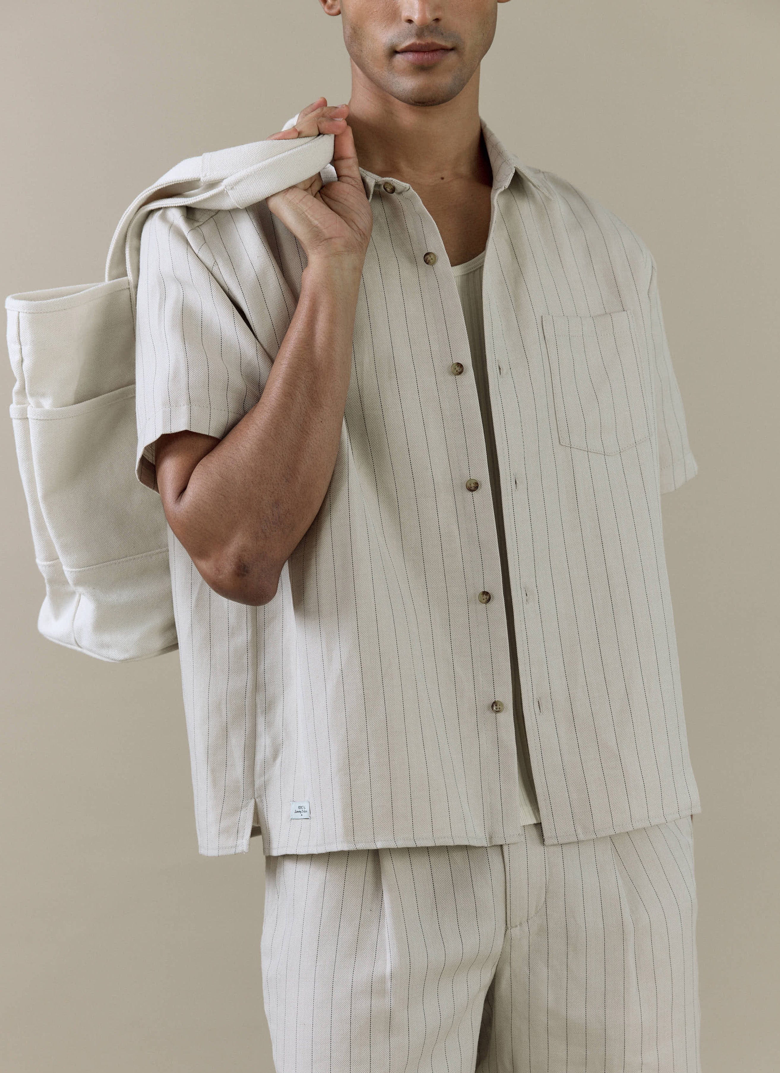 Percival cream striped tailored shorts and matching pinstripe shirt in a linen blend, styled with a tote bag.