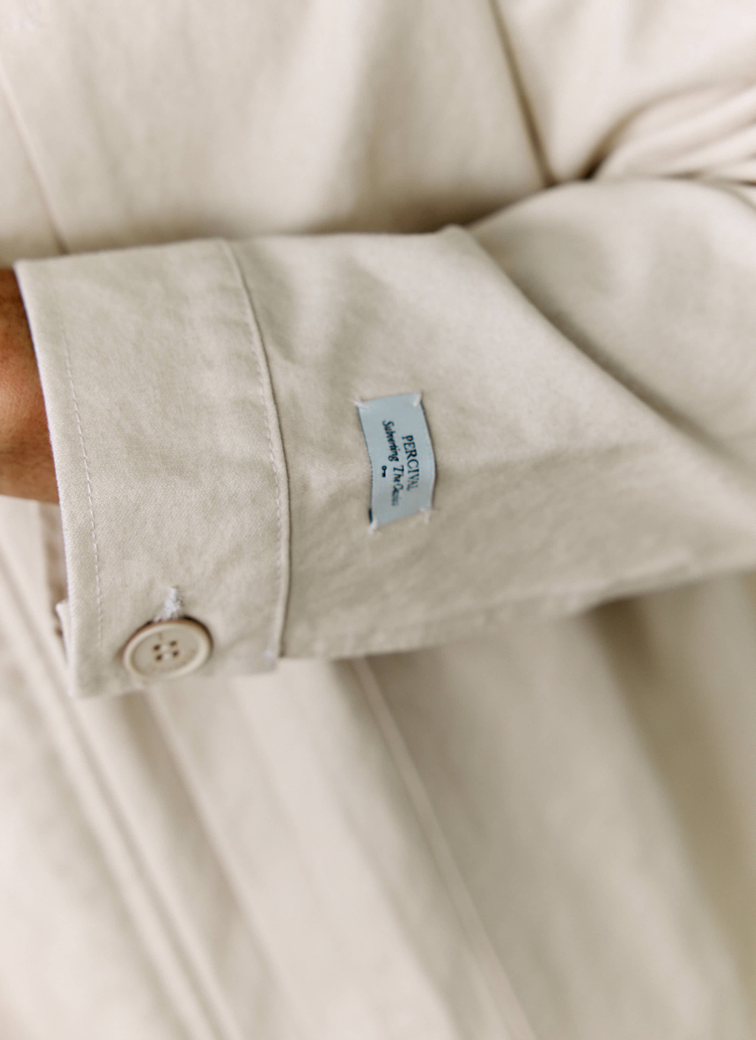 A close-up shot of the branded Percival label on the sleeve of the ecru cotton Ernst Jacket.