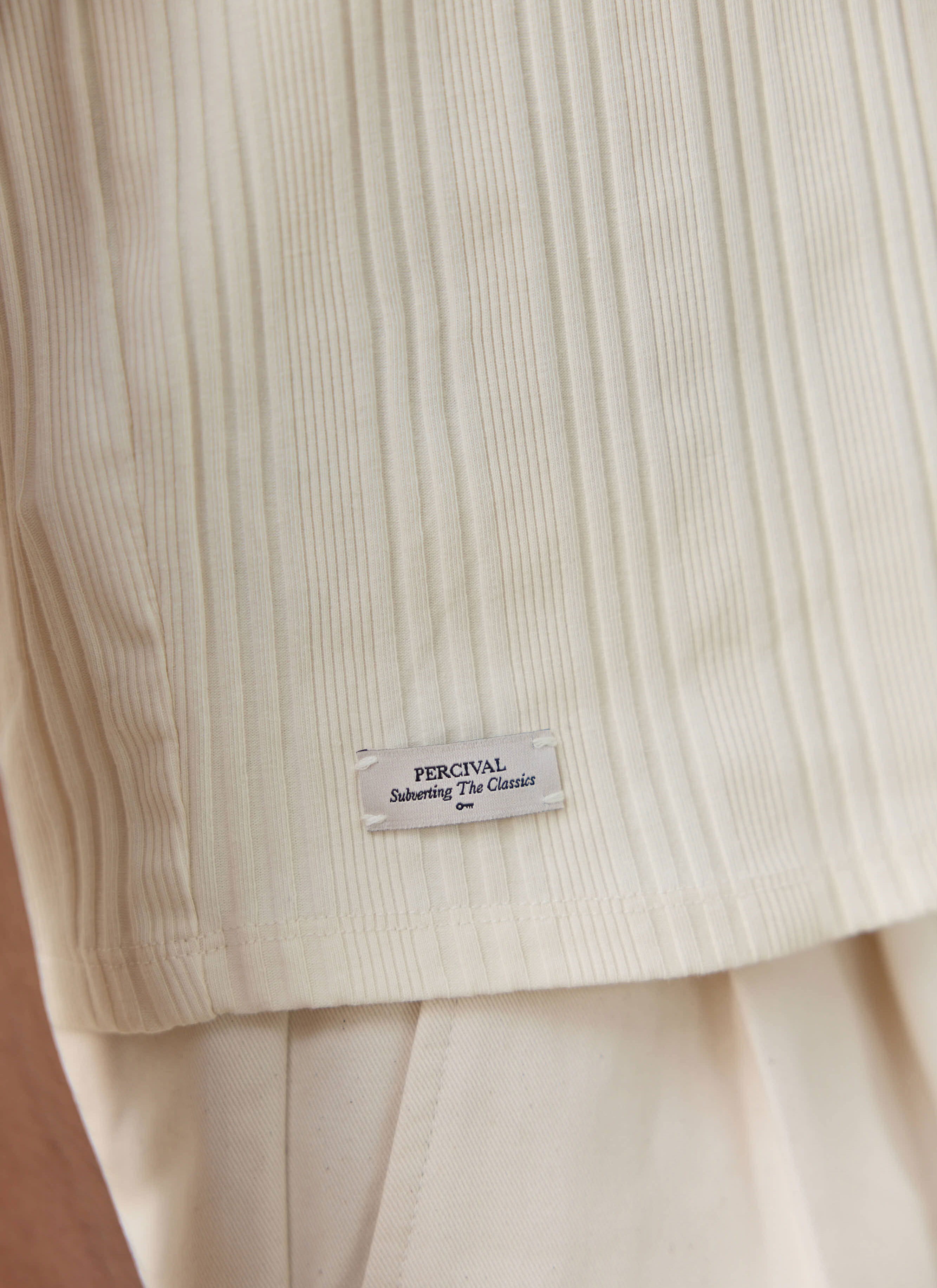 Close-up of the cream ribbed organic cotton Leon Vest by Percival, showing the branded external label at the hem.