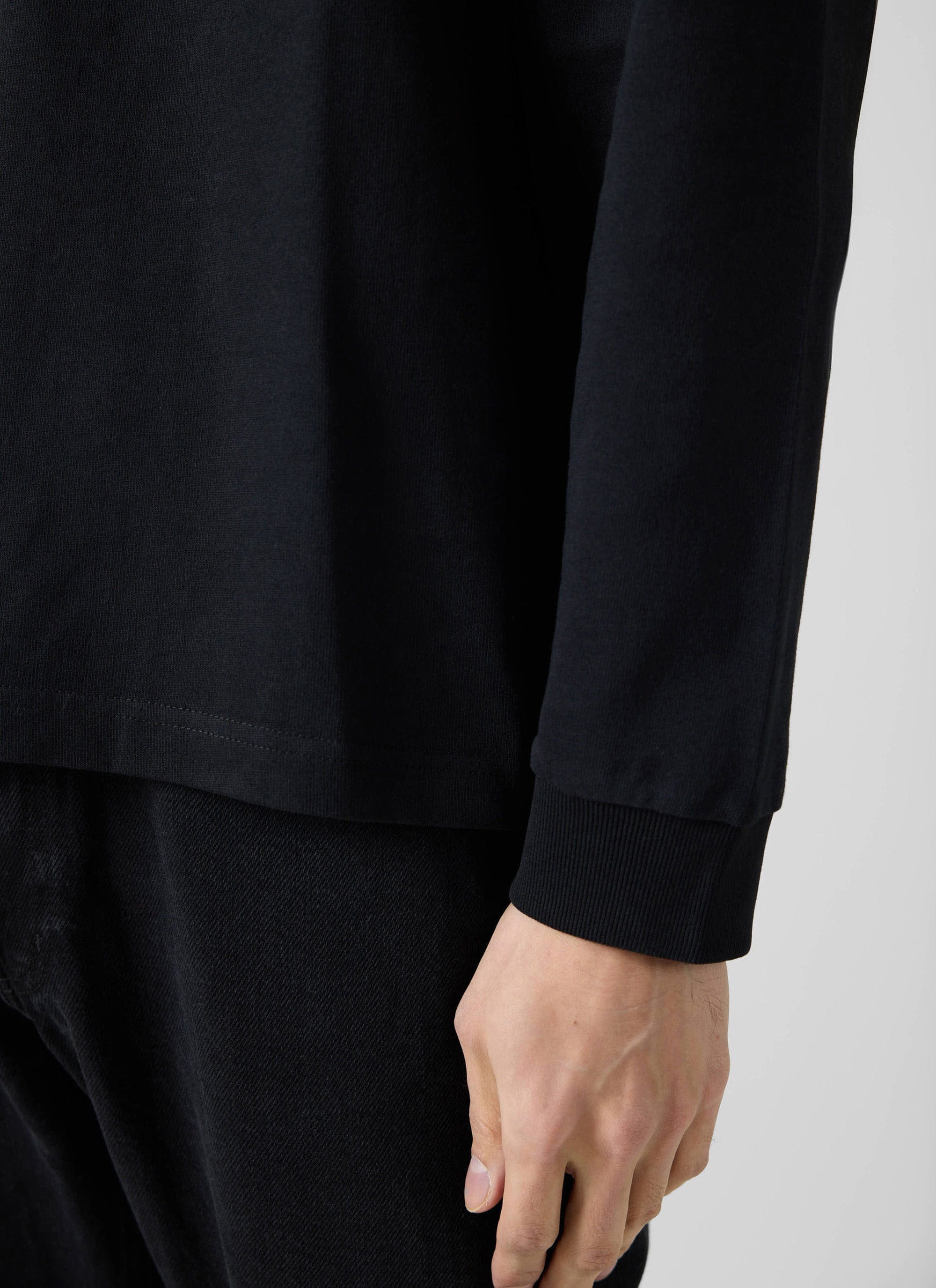 A close-up detail shot of the Percival Long Sleeve Pocket T-Shirt in black, showing the ribbed cuff and hem.