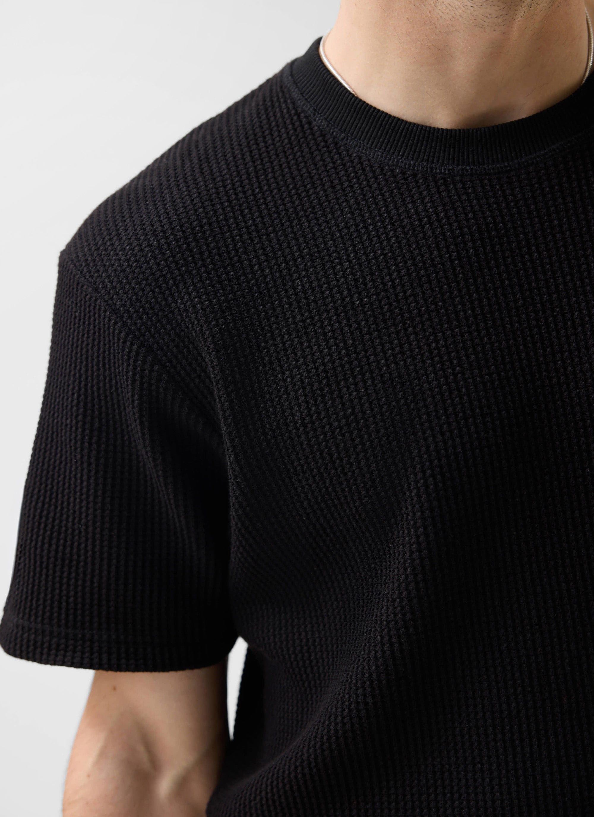 Close-up of a model wearing the Percival Waffle Short Sleeve T-Shirt in black, showing the textured organic cotton knit.