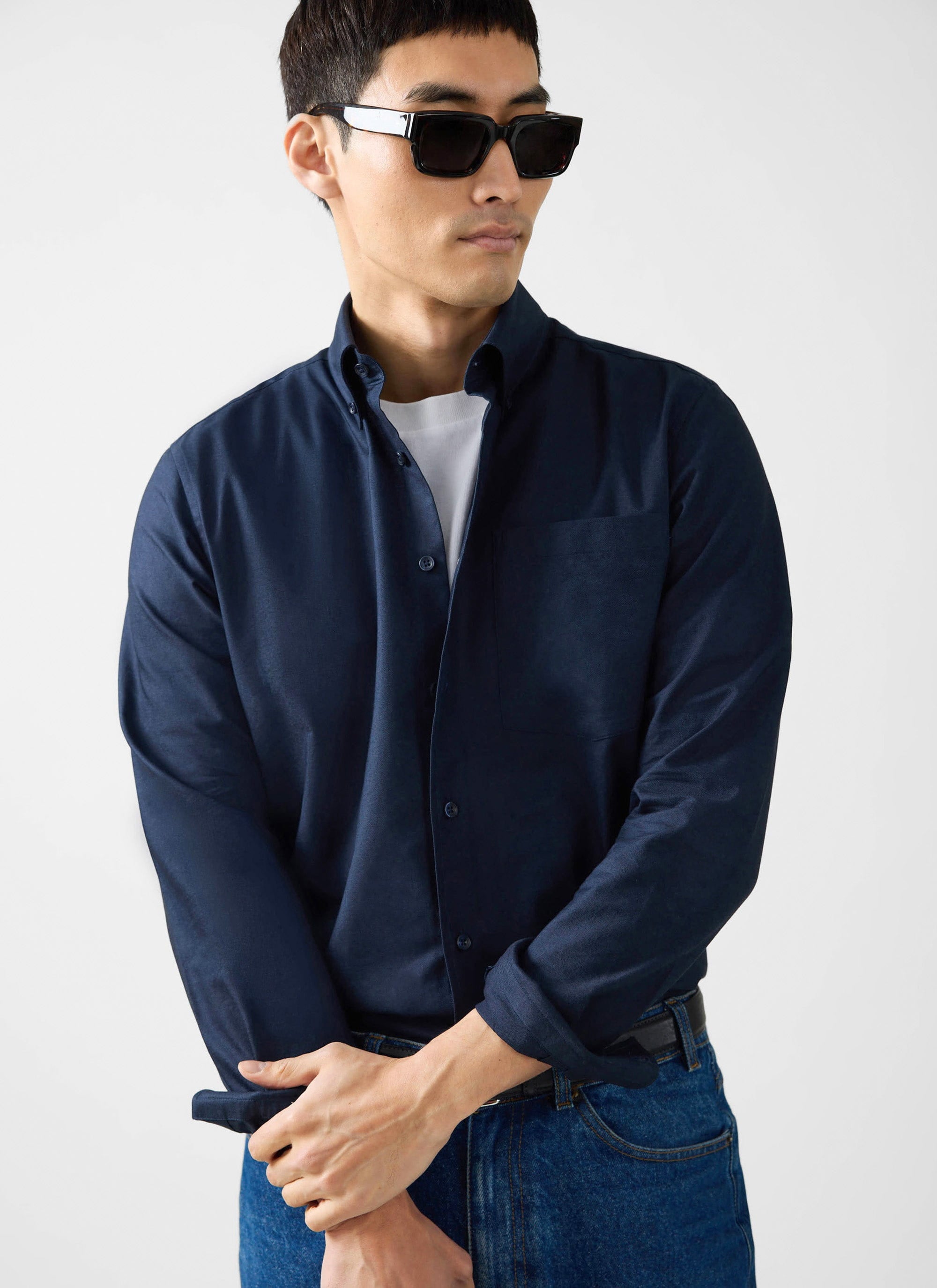 A model wears the navy cotton Oxford Regular Shirt from Percival, styled open over a white tee with jeans and sunglasses.
