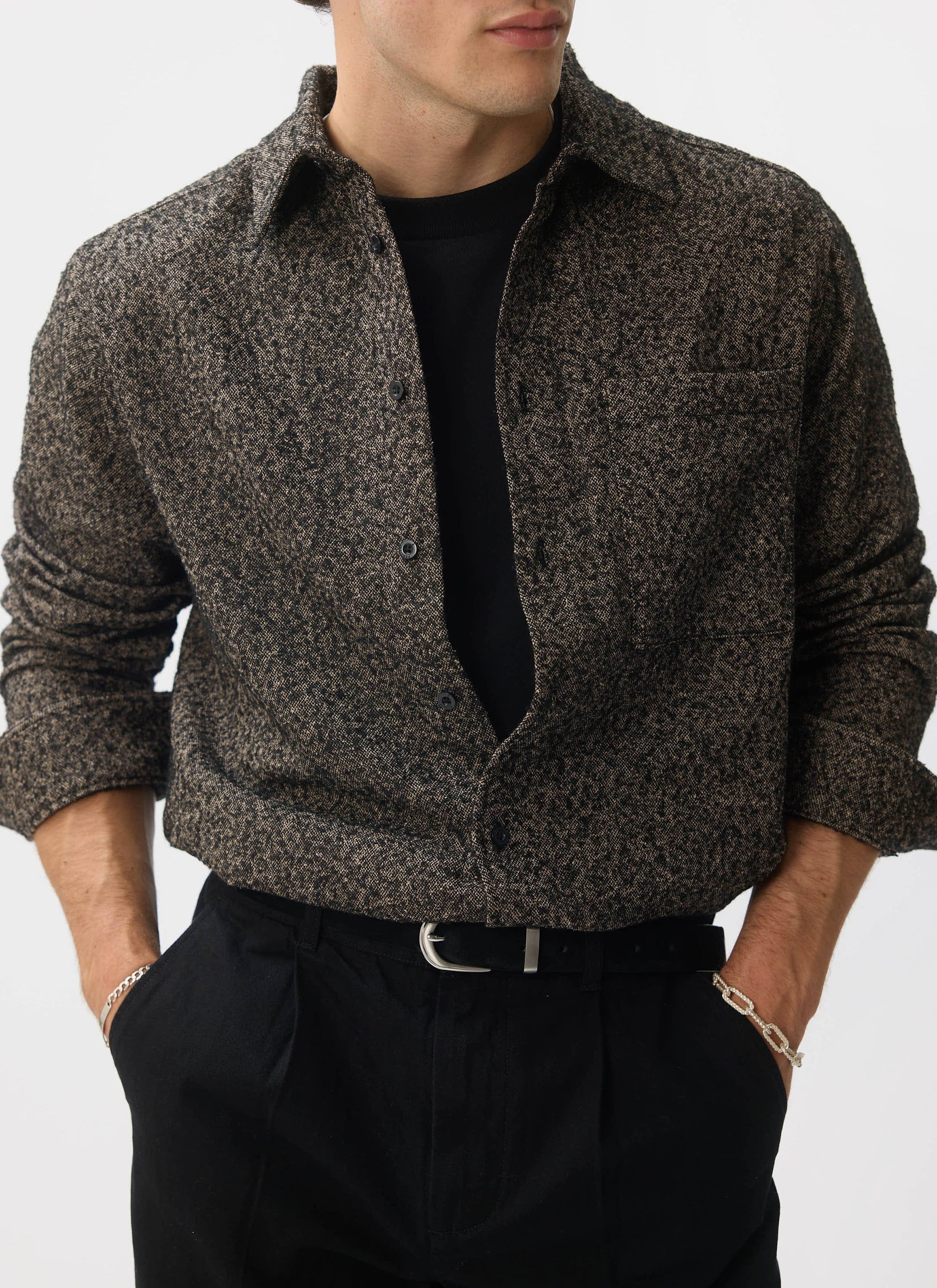 A model wears the Percival Blyton Long Sleeve Shirt in grey, styled open over a black t-shirt and black trousers.