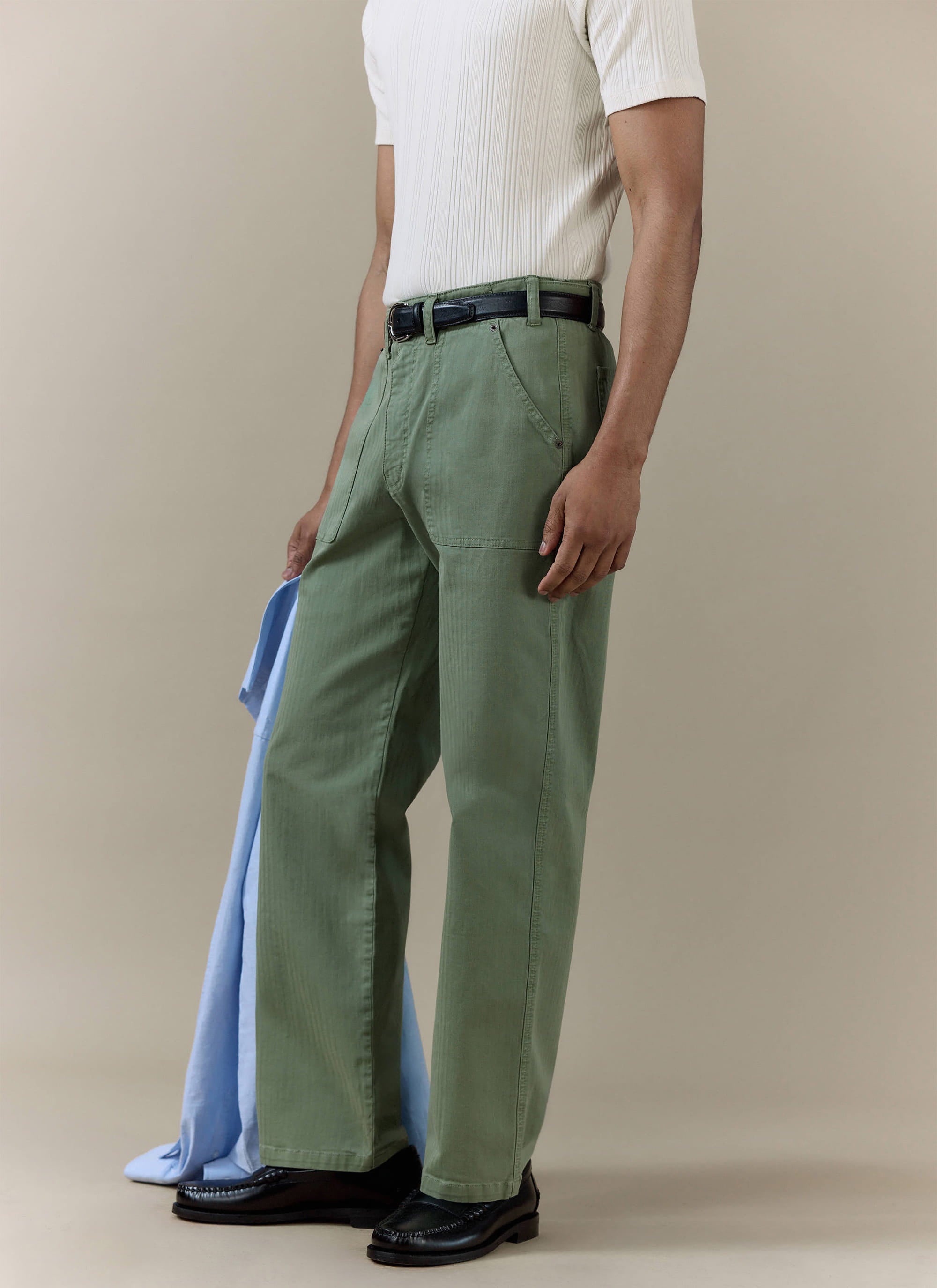 Percival Lungo Herringbone Straight Trousers in sage cotton, styled with a white ribbed shirt and black loafers.