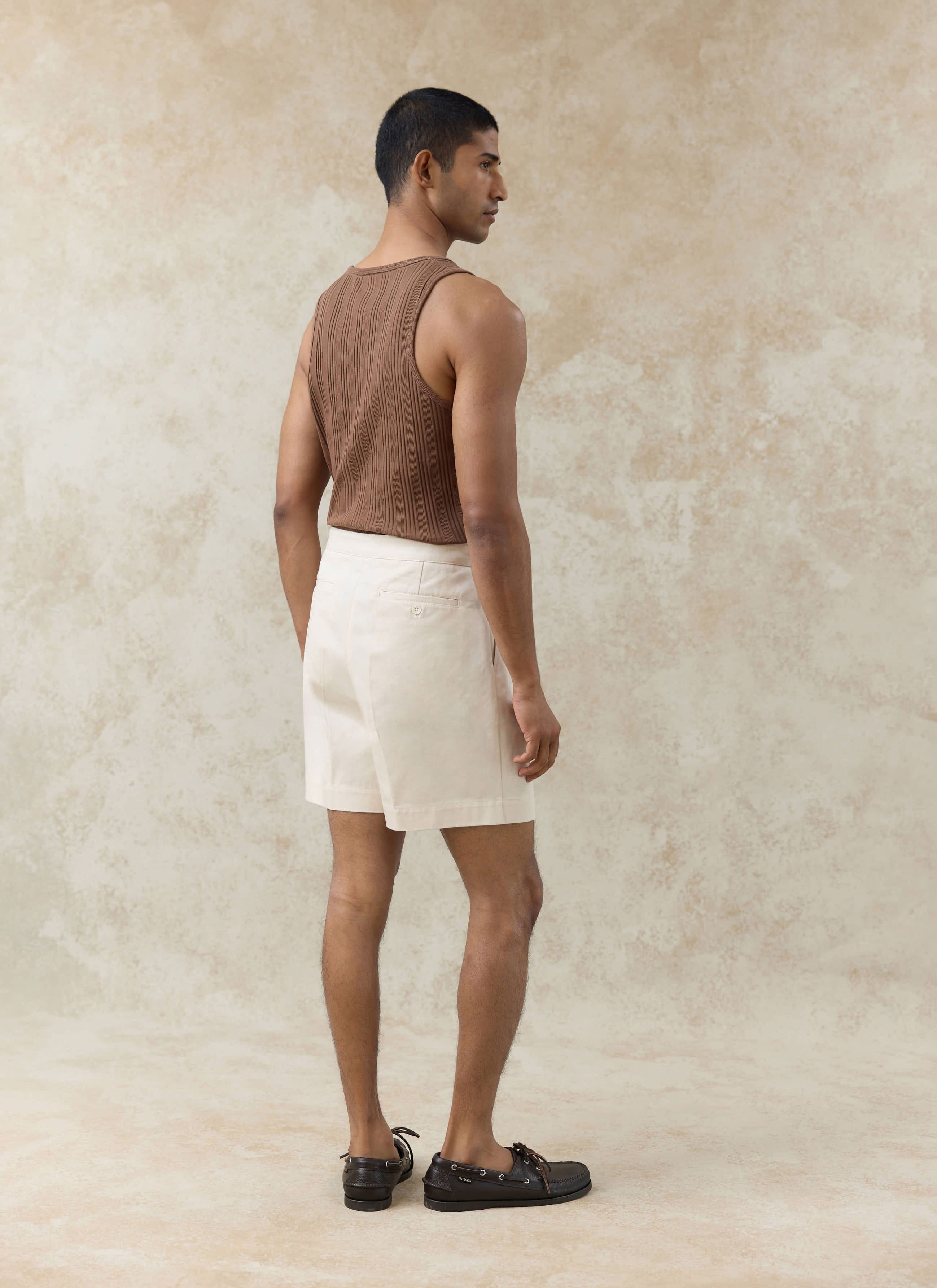 Cream cotton Blake double pleated shorts and a brown Leon ribbed vest by Percival, shown from the rear on a model.