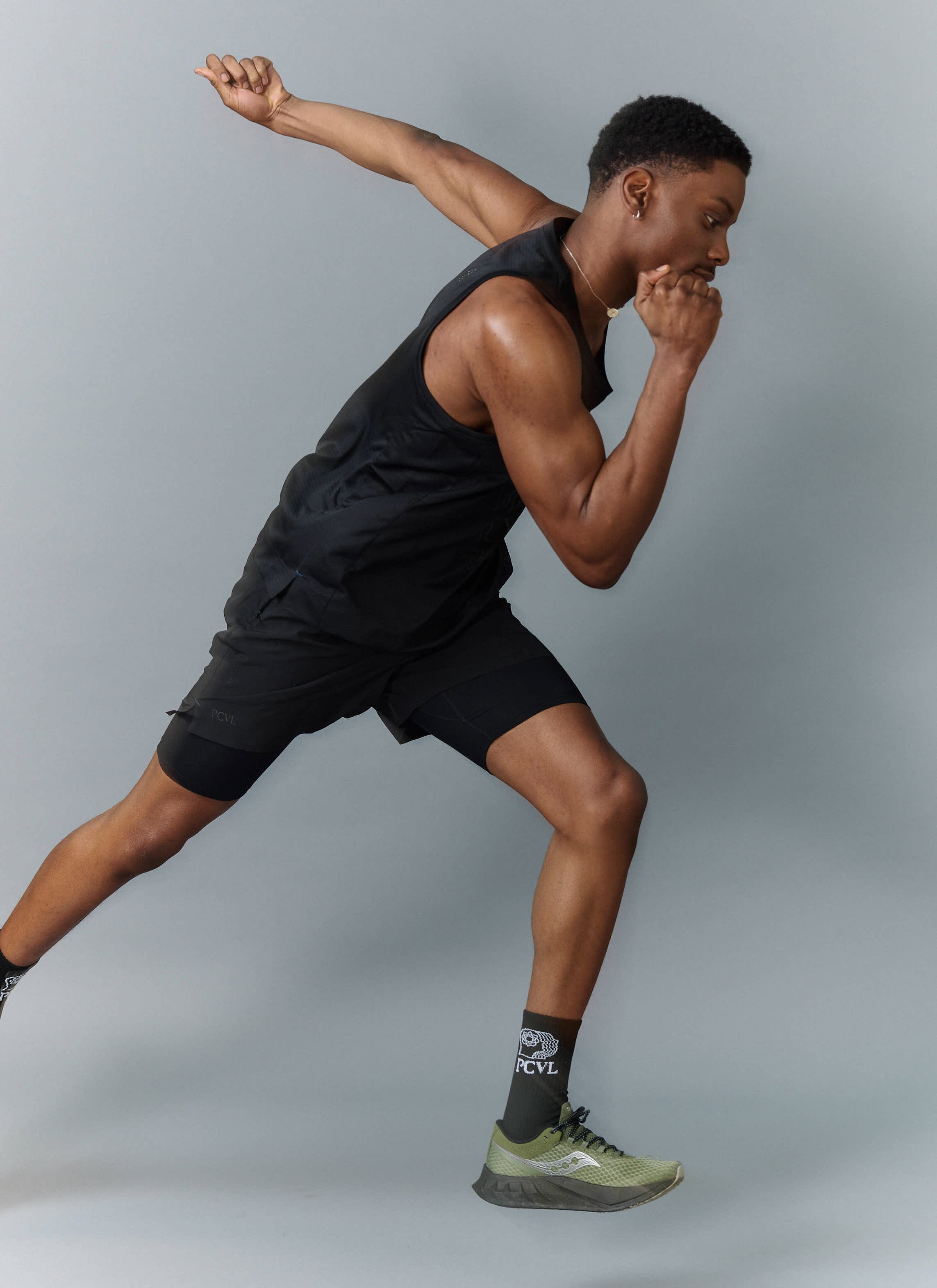 A model wears the black PCVL Performance Vest from Percival, styled with matching PCVL shorts and socks in a running pose.