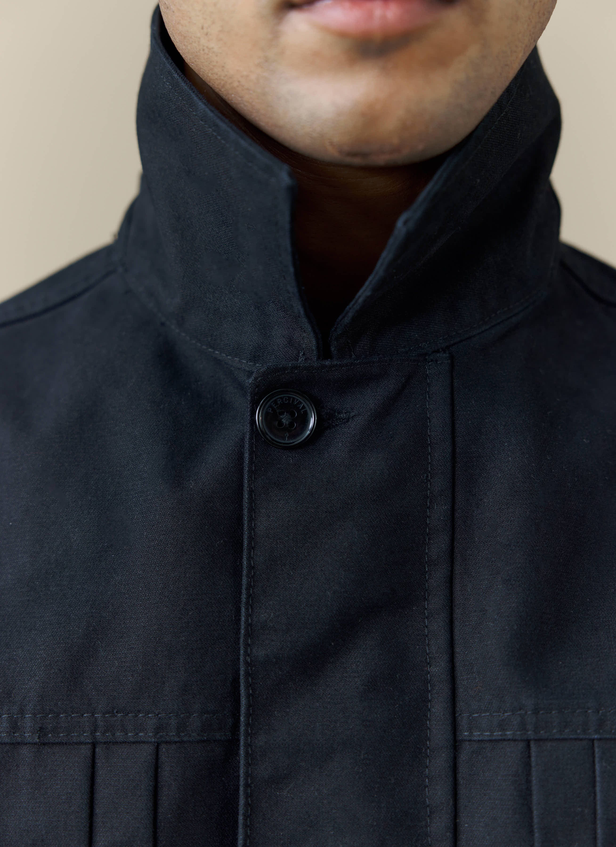 A close-up of the collar and branded button on the black cotton Ernst Jacket from Percival.