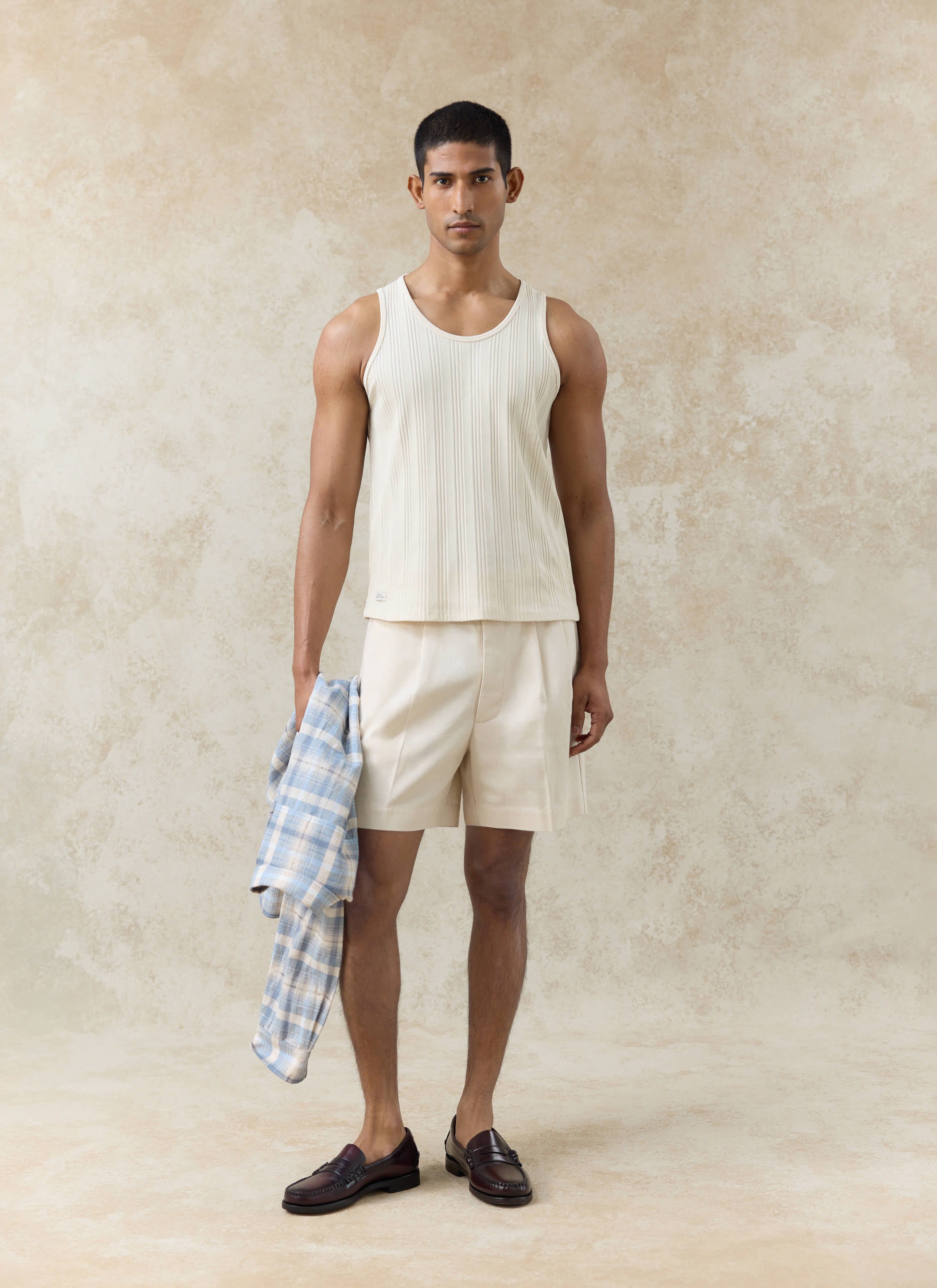 Percival Leon Ribbed Vest and cream Blake Double Pleated Shorts worn by a model holding a blue checked shirt.