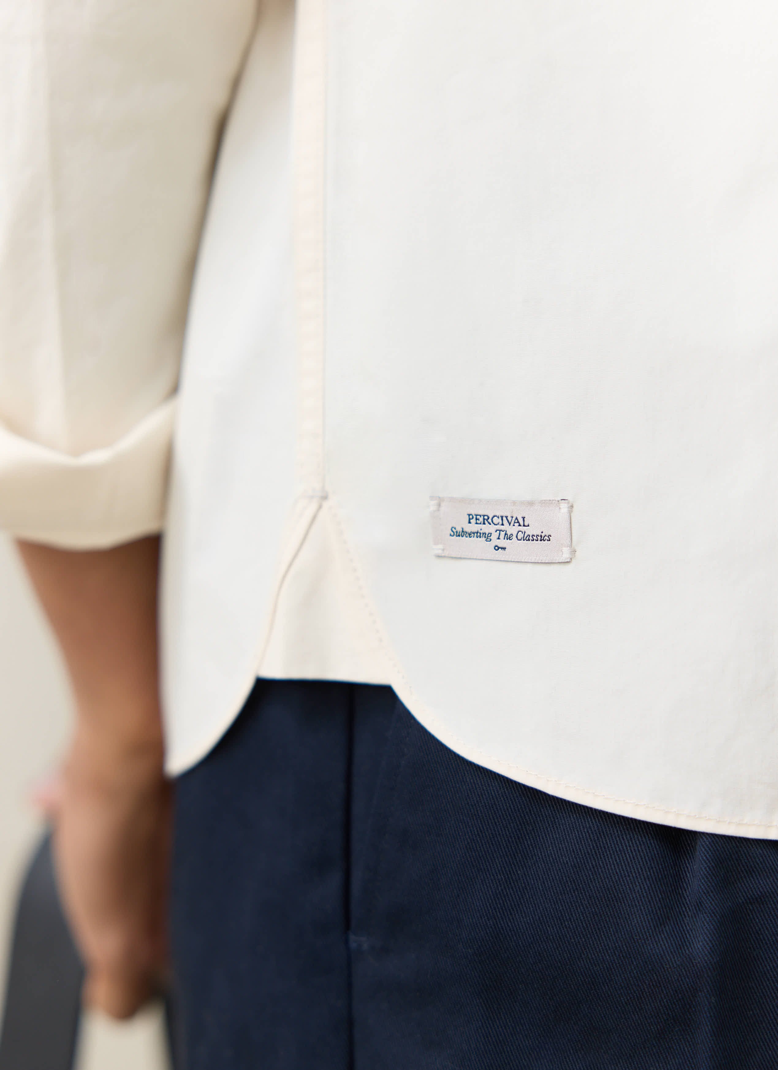 Close-up of the cream cotton Percival Dali Relaxed Poplin Shirt hem, featuring the branded label and curved seam.