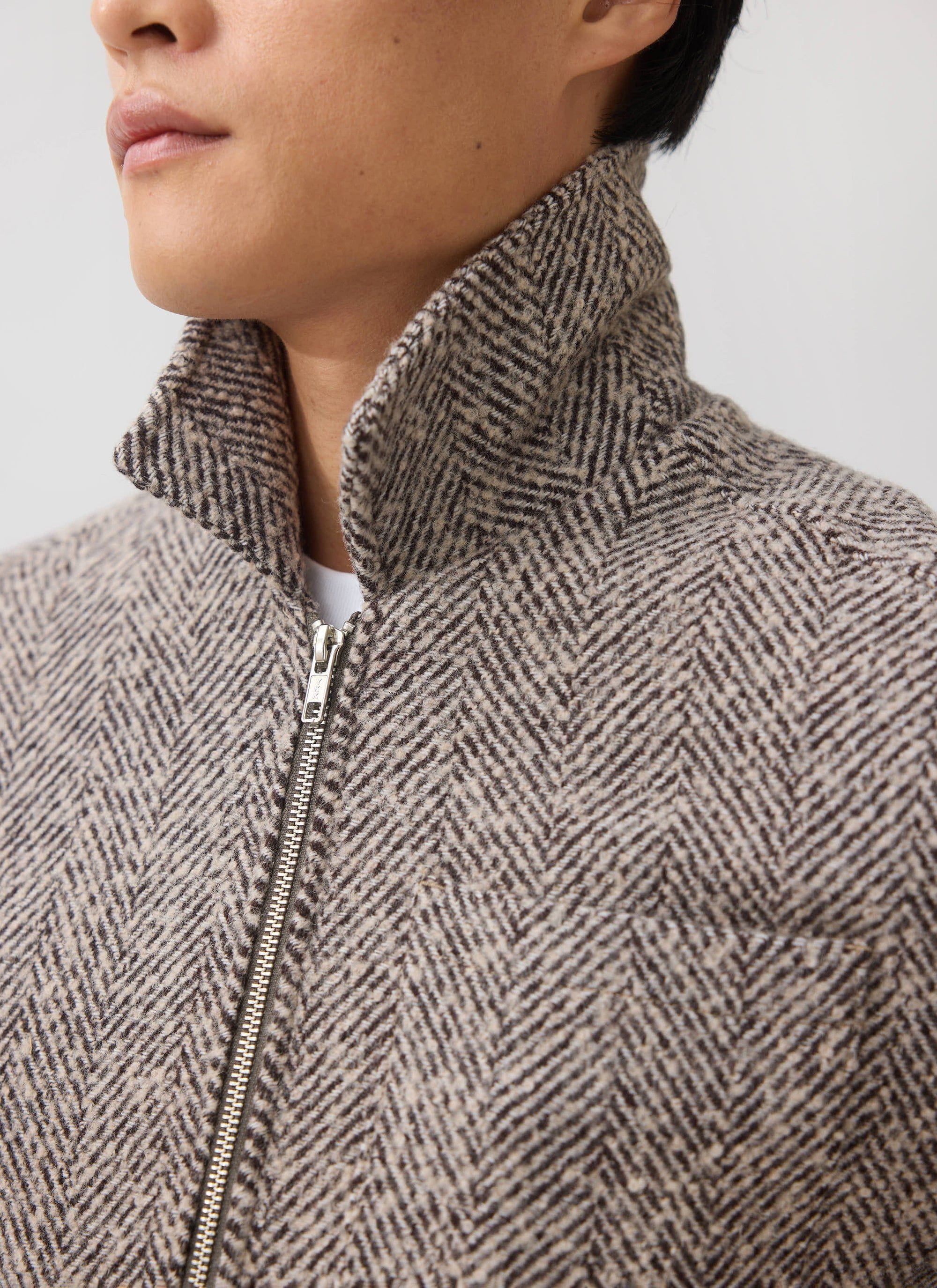 A close-up of a model wearing the Percival Herringbone Zip Jacket in ecru wool, showing the collar and zip detail.