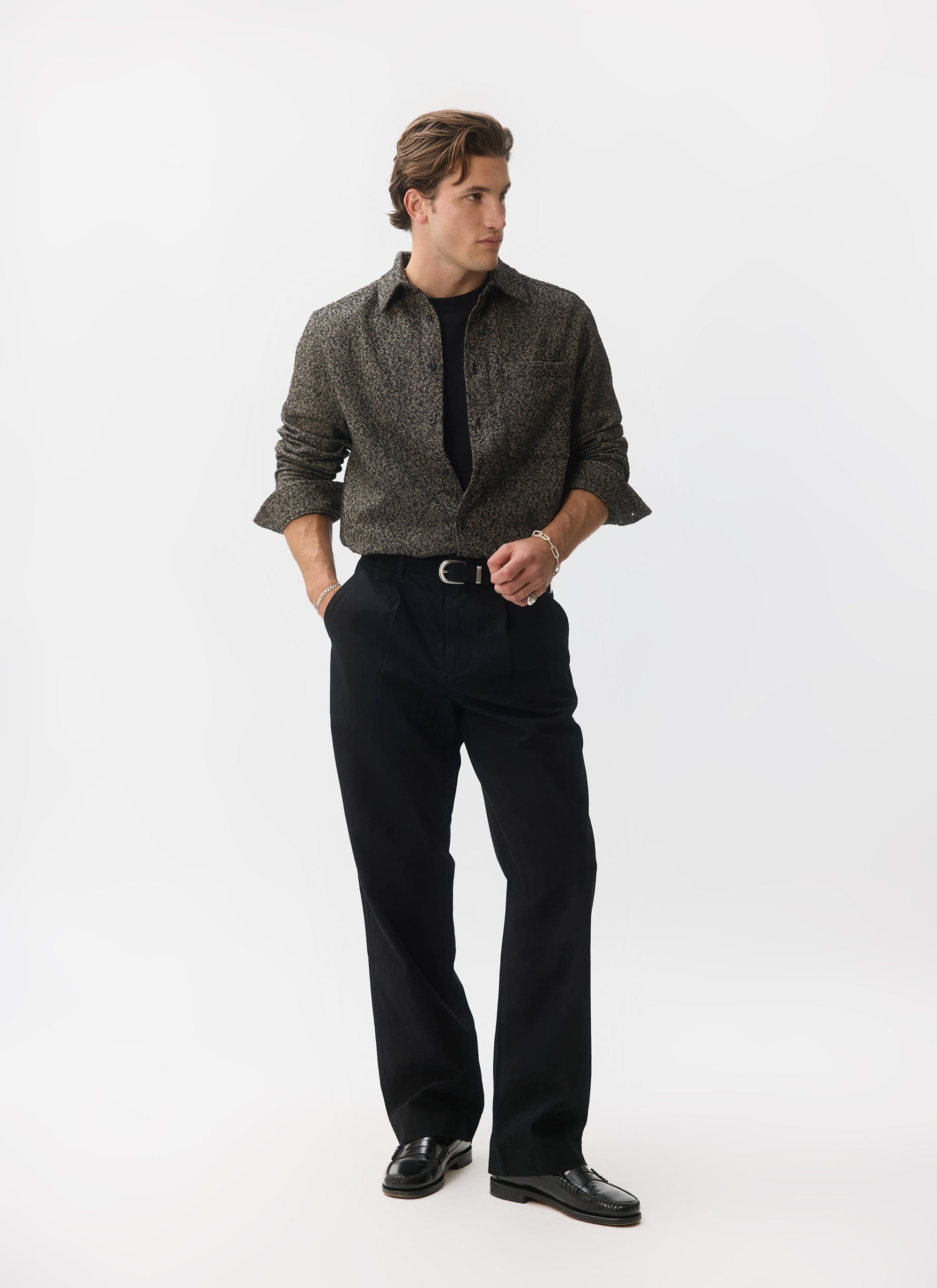 A man models the Percival Blyton Long Sleeve Shirt in grey, styled over a black t-shirt with smart black trousers.