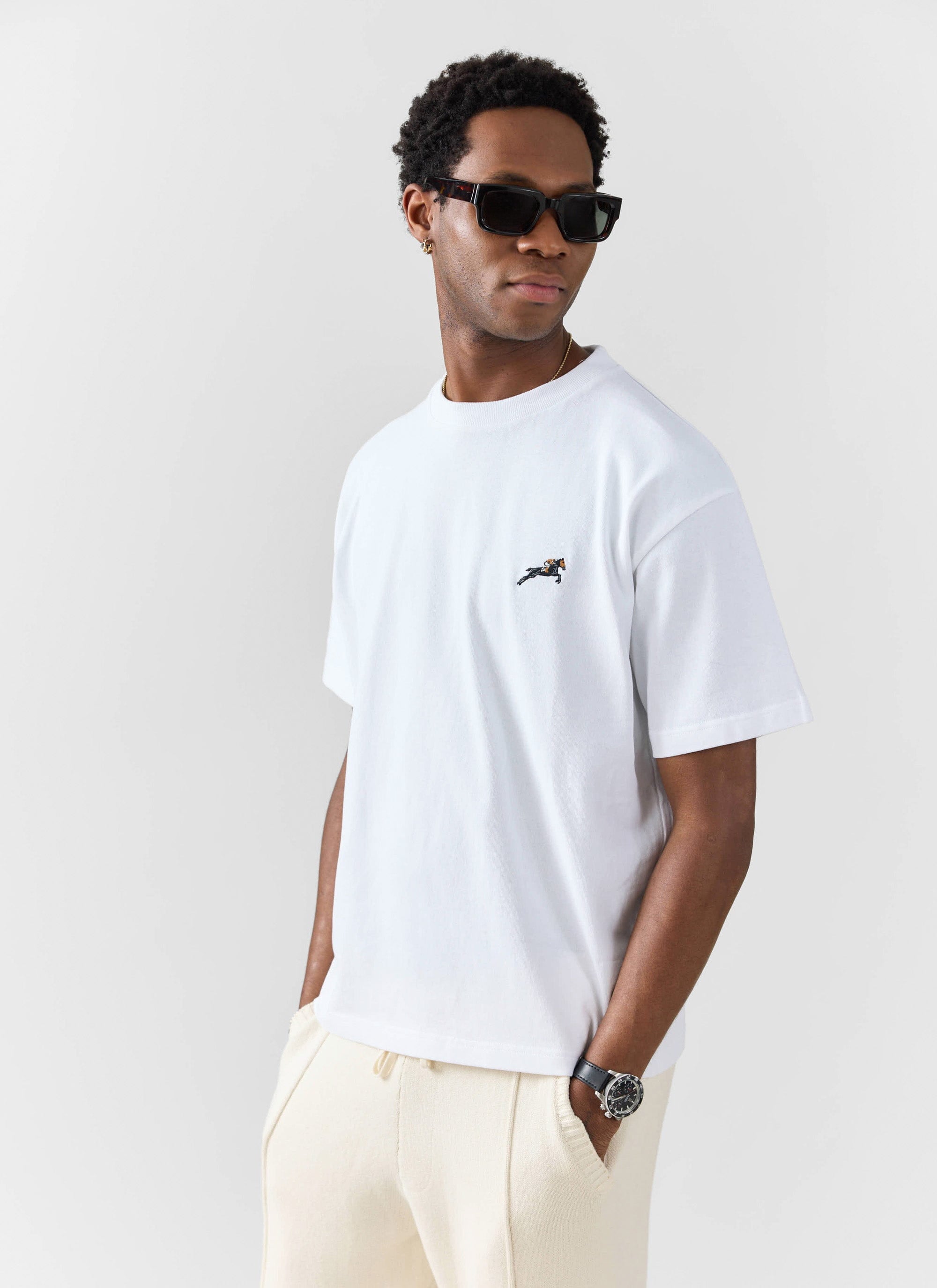 A man models the white Galloping Horse embroidered t-shirt from Percival, styled with cream trousers and sunglasses.